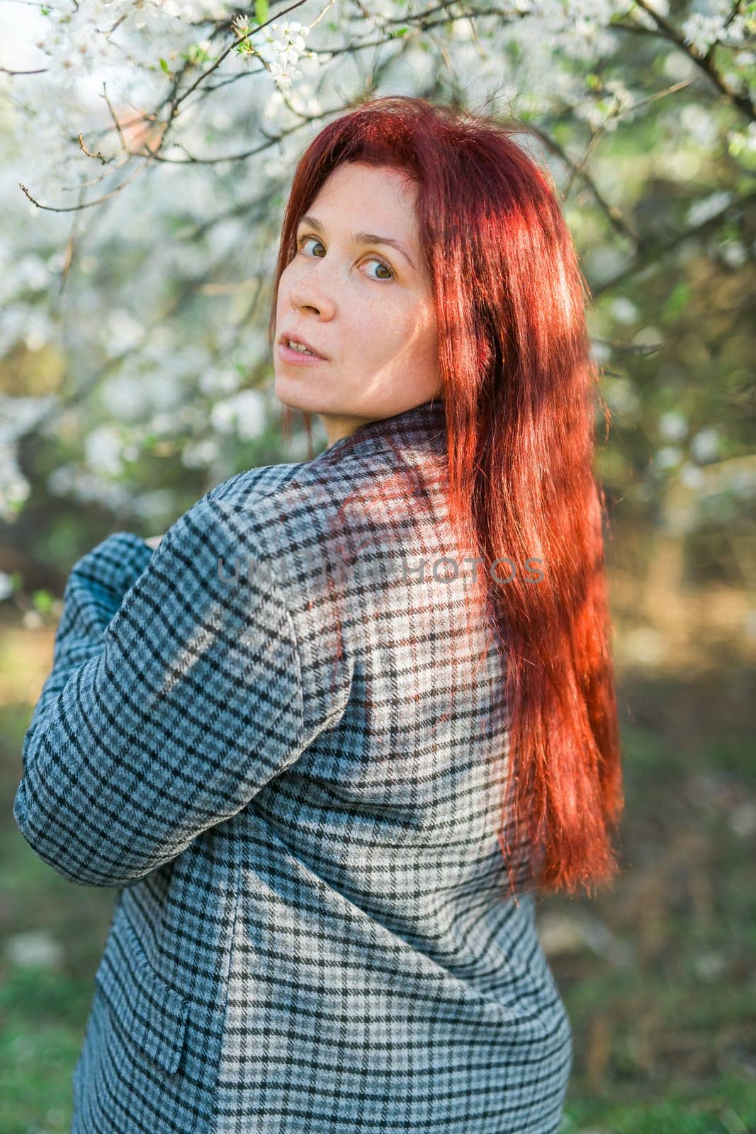 Beautiful red-haired woman enjoying smell in a flowering blooming spring garden. Spring blossom by Satura86