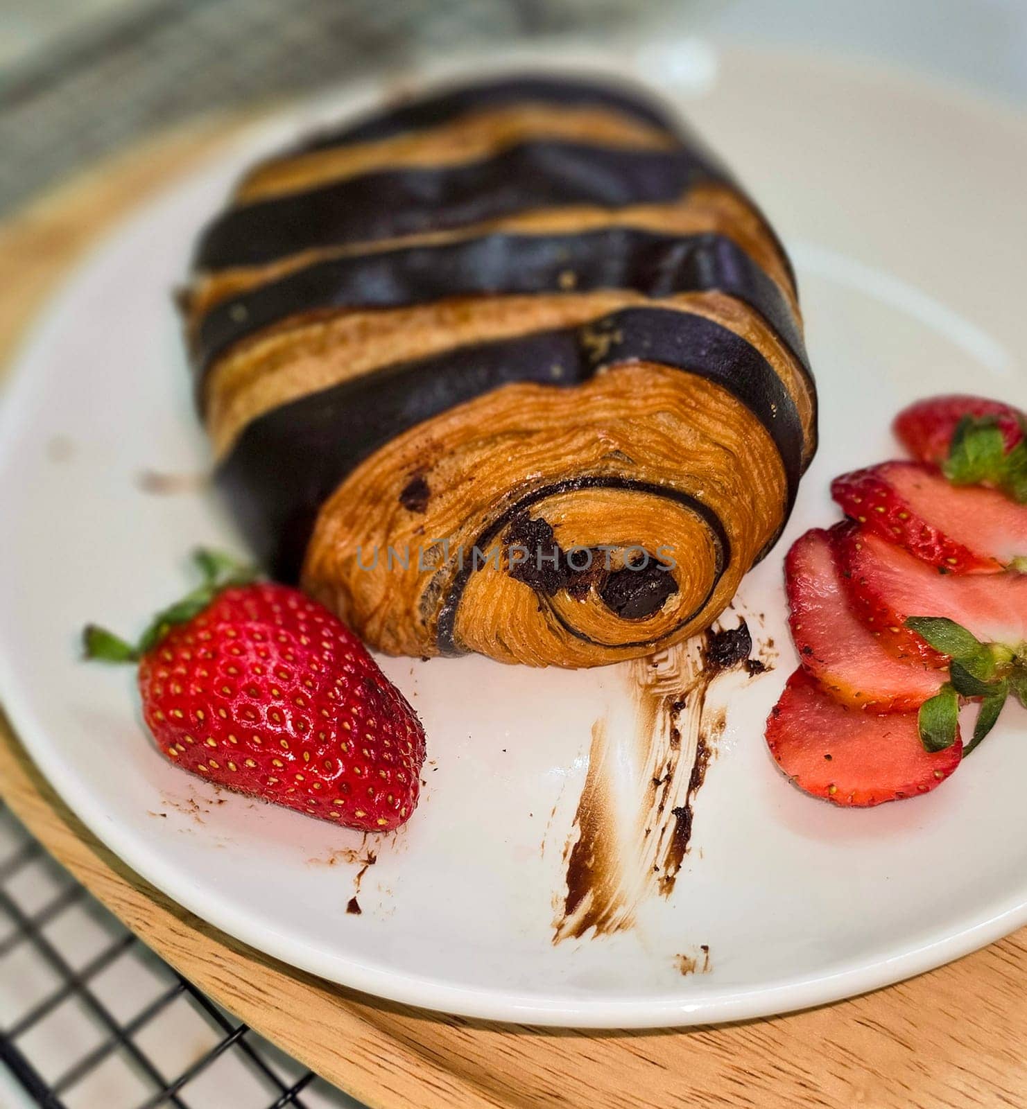 Fresh homemade striped chocolate croissant with chocolate filling on a round white plate, served with fresh strawberry, good cooking ideas