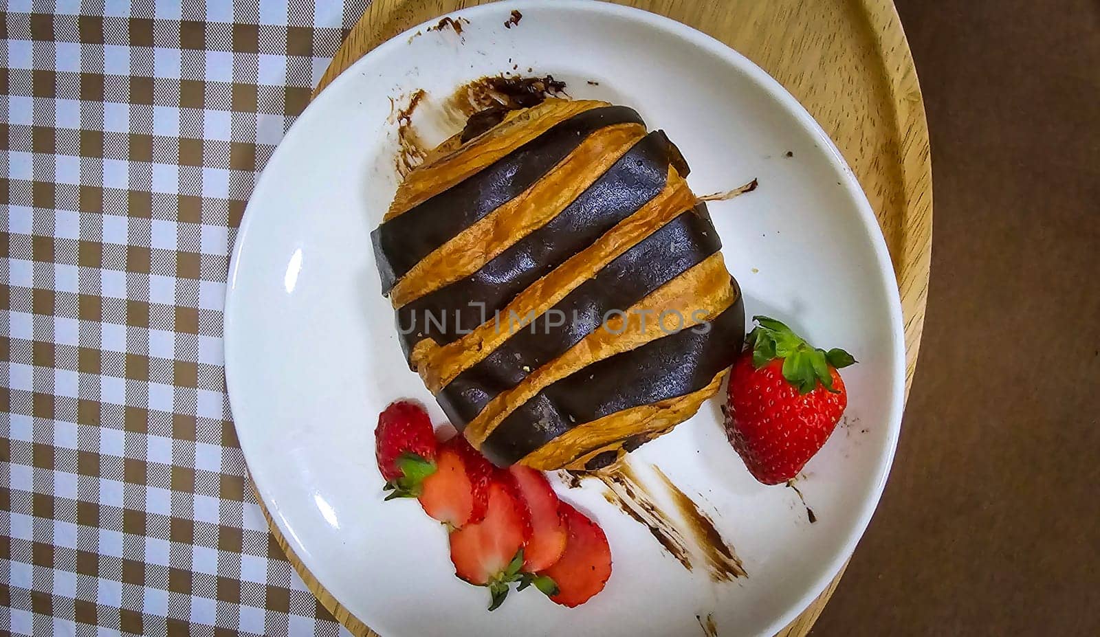 Fresh homemade striped chocolate croissant with chocolate filling on a round white plate, served with fresh strawberry by antoksena