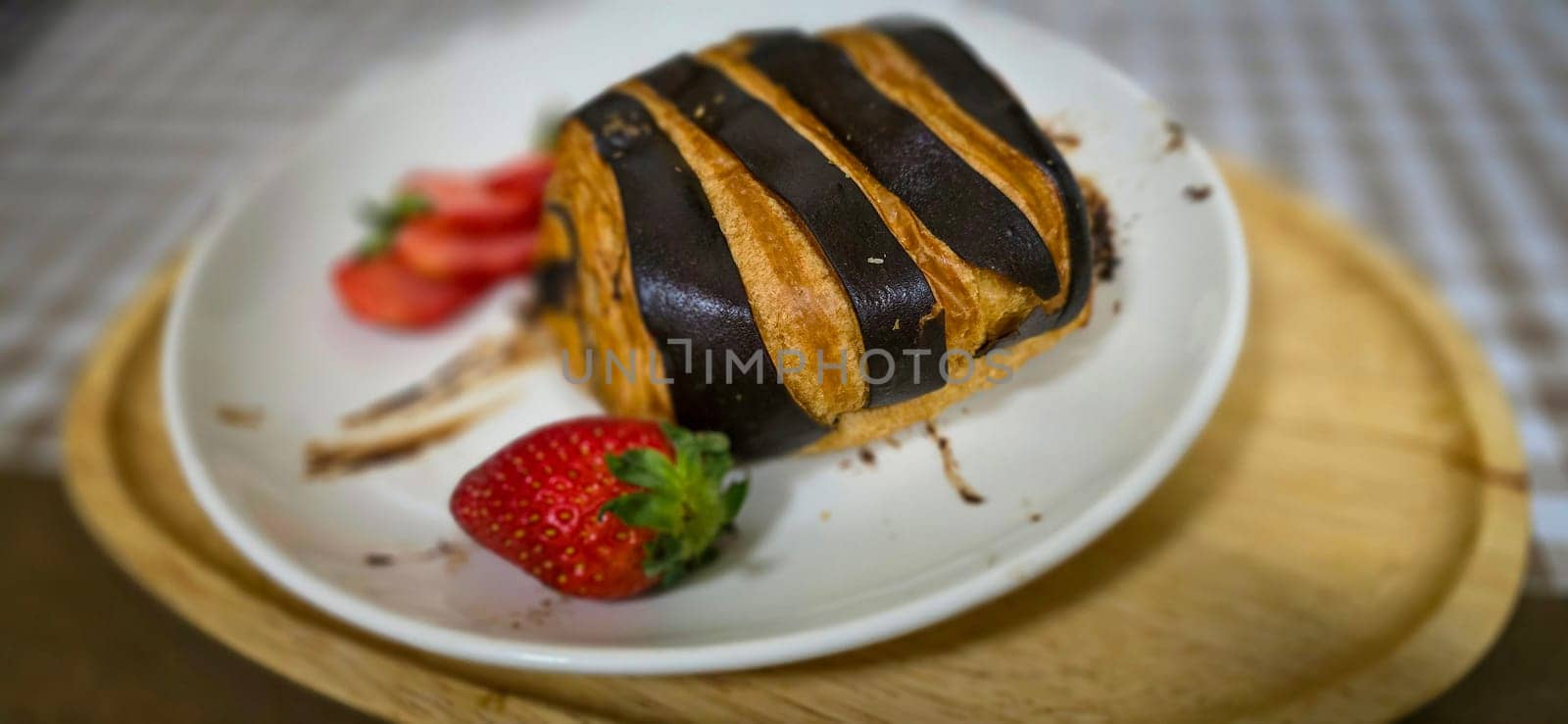 Fresh homemade striped chocolate croissant with chocolate filling on a round white plate, served with fresh strawberry, good cooking ideas