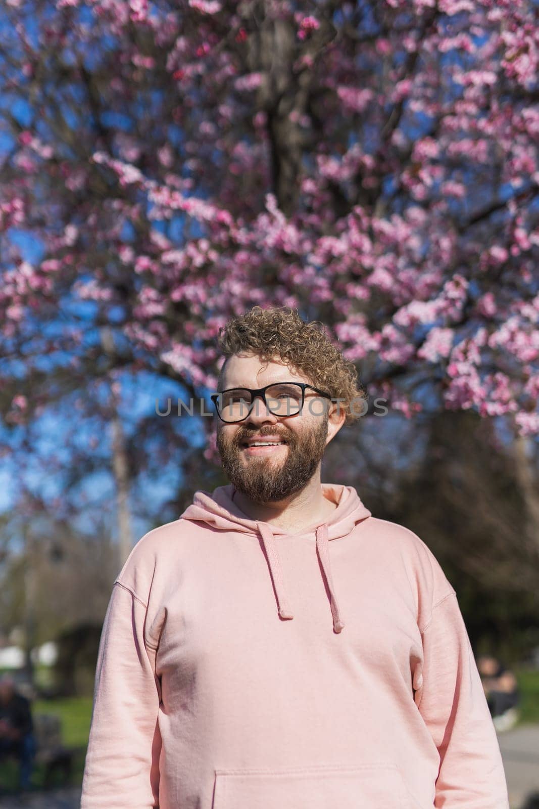 Man allergic enjoying after treatment from seasonal allergy at spring. Portrait of happy bearded man smiling in front of blossom tree at springtime. Spring blooming and allergy concept. Copy space, vertical by Satura86