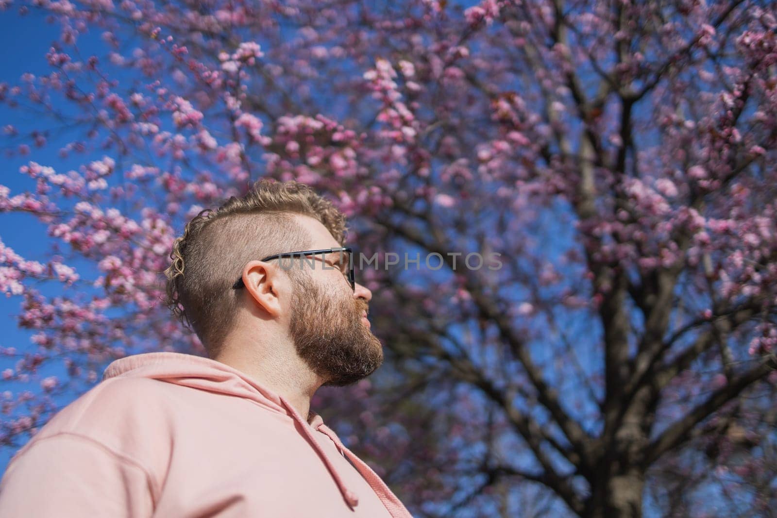 Man allergic enjoying after treatment from seasonal allergy at spring. Portrait of happy bearded man smiling in front of blossom tree at springtime. Spring blooming and allergy concept. Copy space.