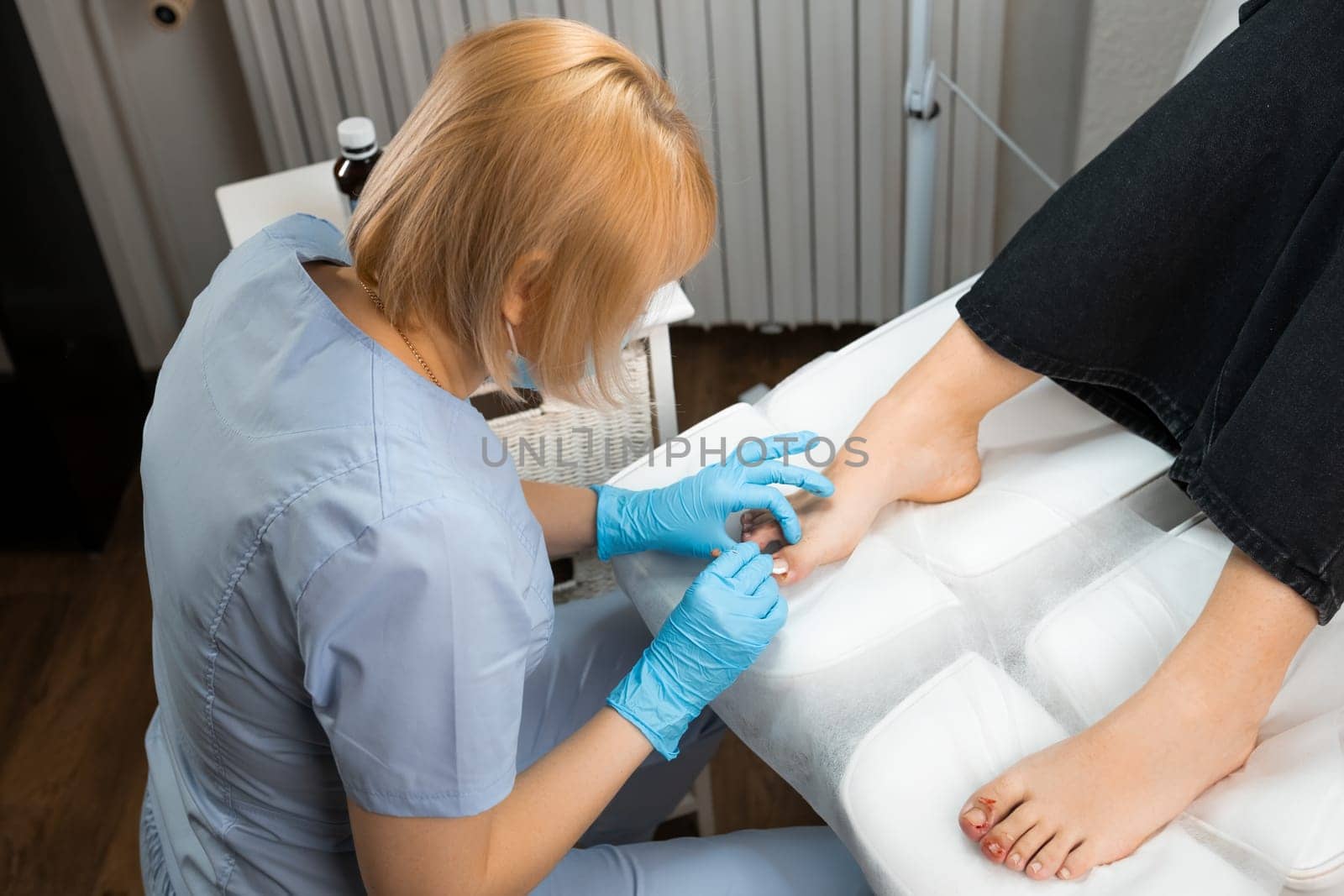 Top view of female podiatrist performs the procedure of ingrown nail removal using nippers.
