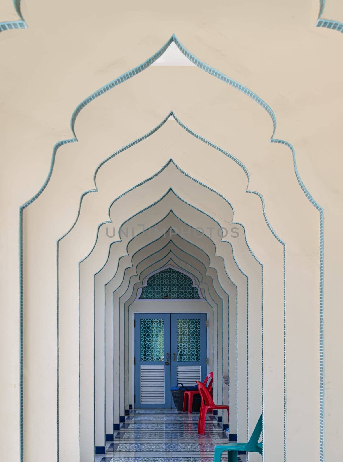 Bangkok, Thailand - Apr 15, 2024 - Interior diminishing perspective view of hallway along with gable partitions wall and plastic chairs inside Bang O mosque leading into entrance blue door. Mosque architecture and art concept, Space for text, Selective focus.