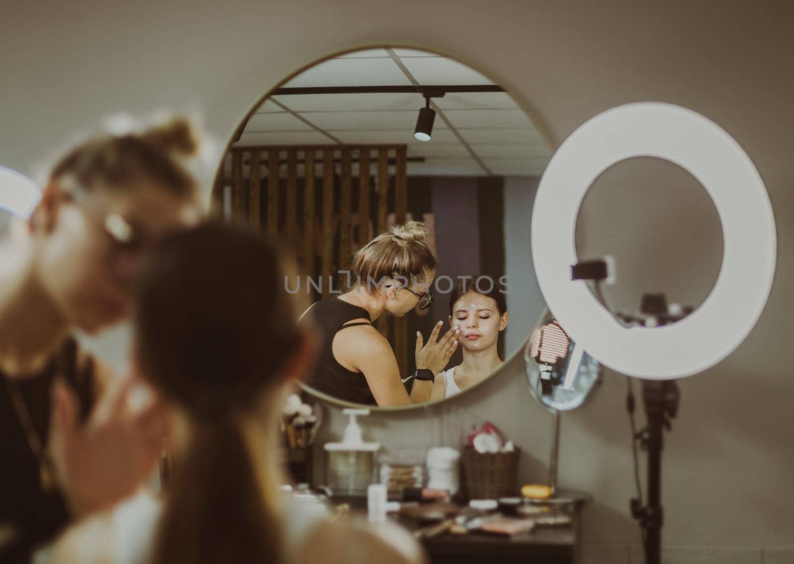 A young makeup artist applies protective cream to a girl s face. by Nataliya