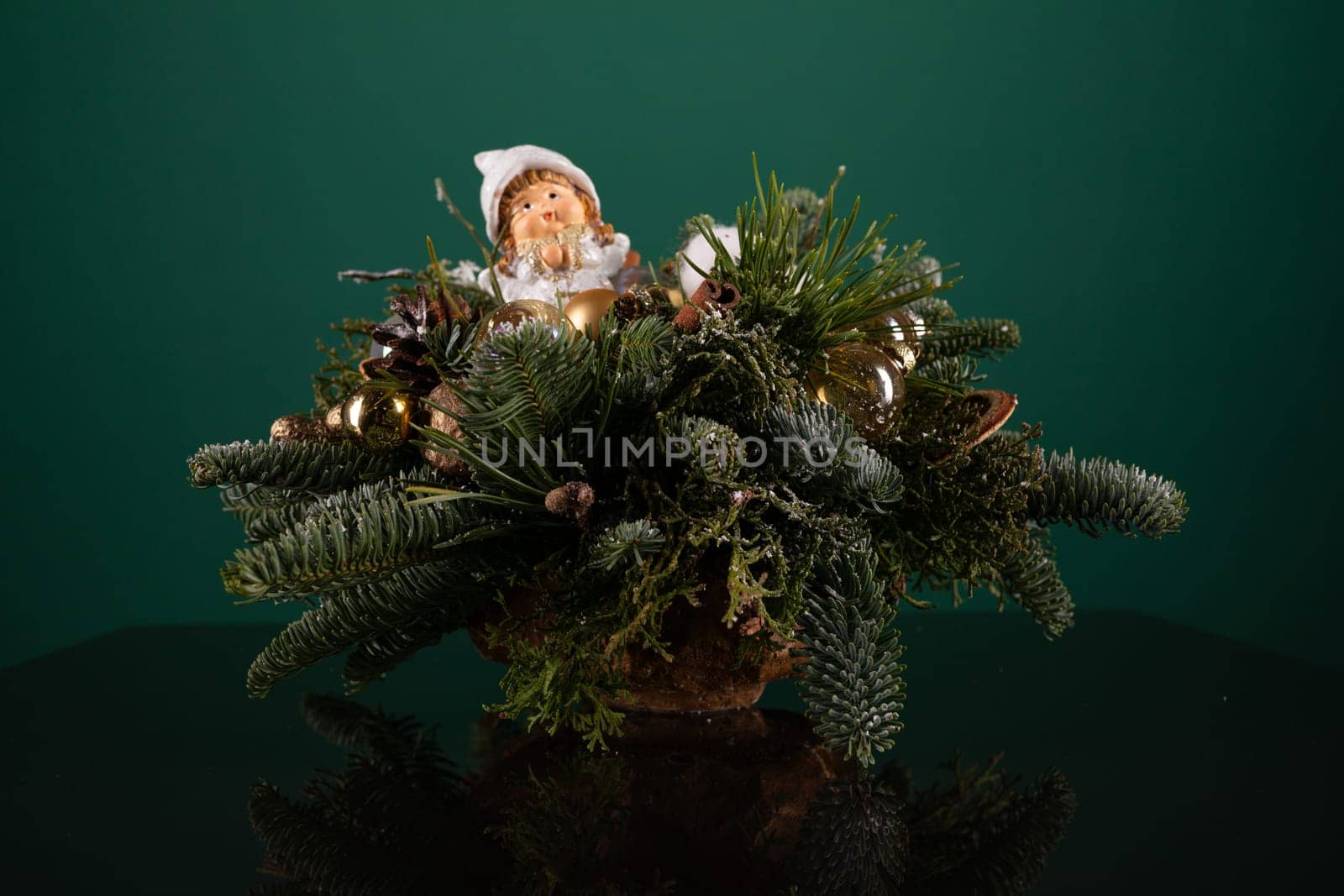 A potted plant with vibrant green leaves has a small doll placed on its soil-filled pot. The doll is motionless, sitting upright on the edge of the pot, adding a whimsical touch to the plants display.