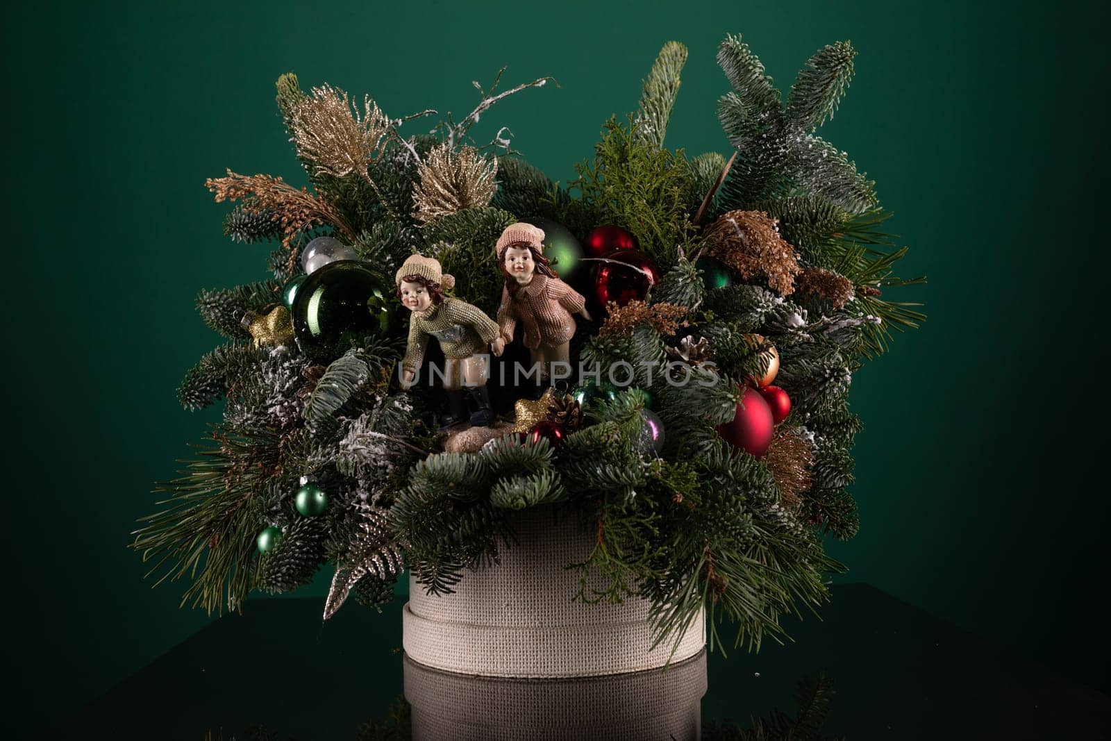 A festive holiday arrangement featuring cuddly teddy bears and sparkling ornaments in red, green, and gold colors. The teddy bears are wearing Santa hats and the ornaments are delicately placed around them.