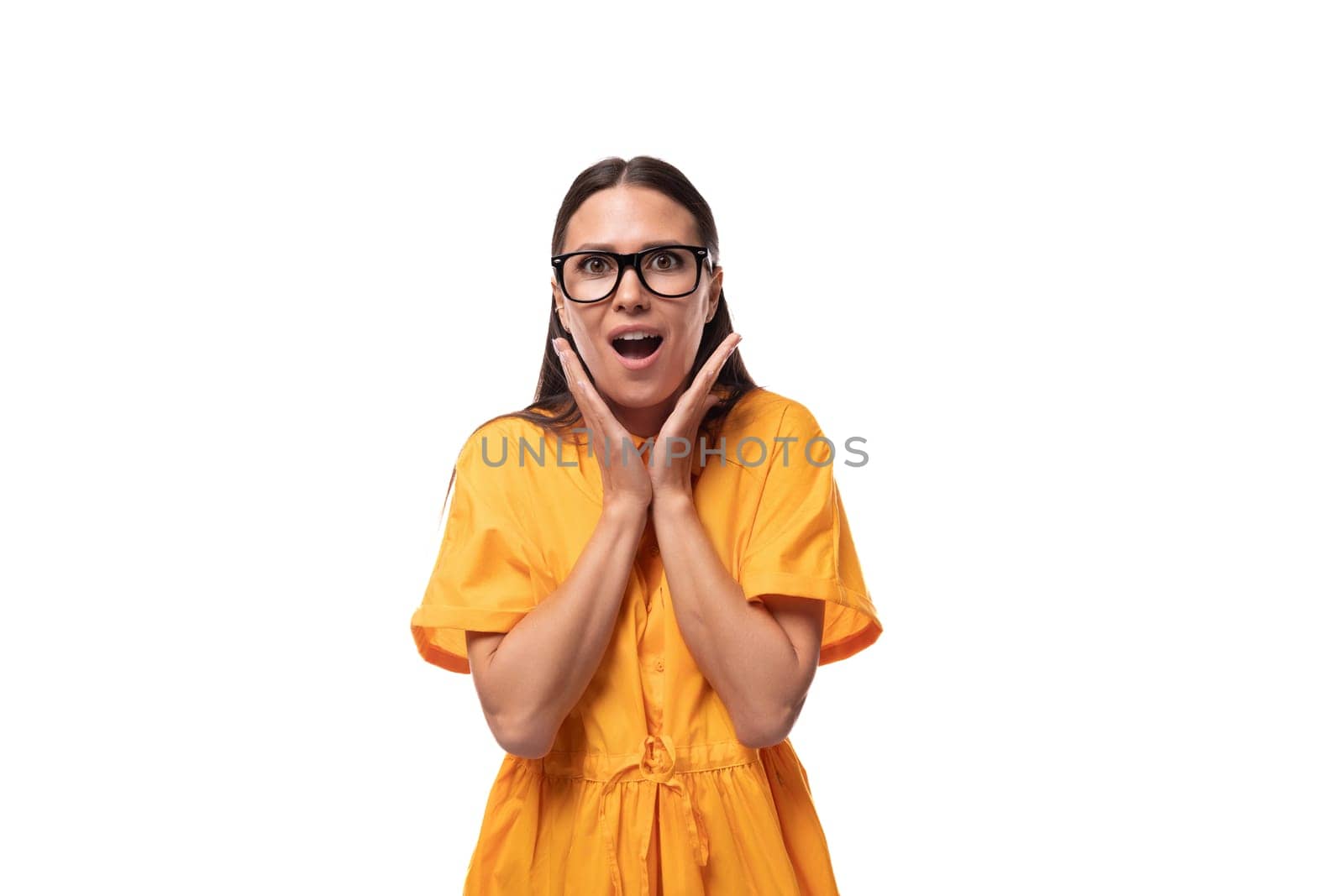 young pretty brunette lady dressed in a yellow dress looks at the camera in surprise.