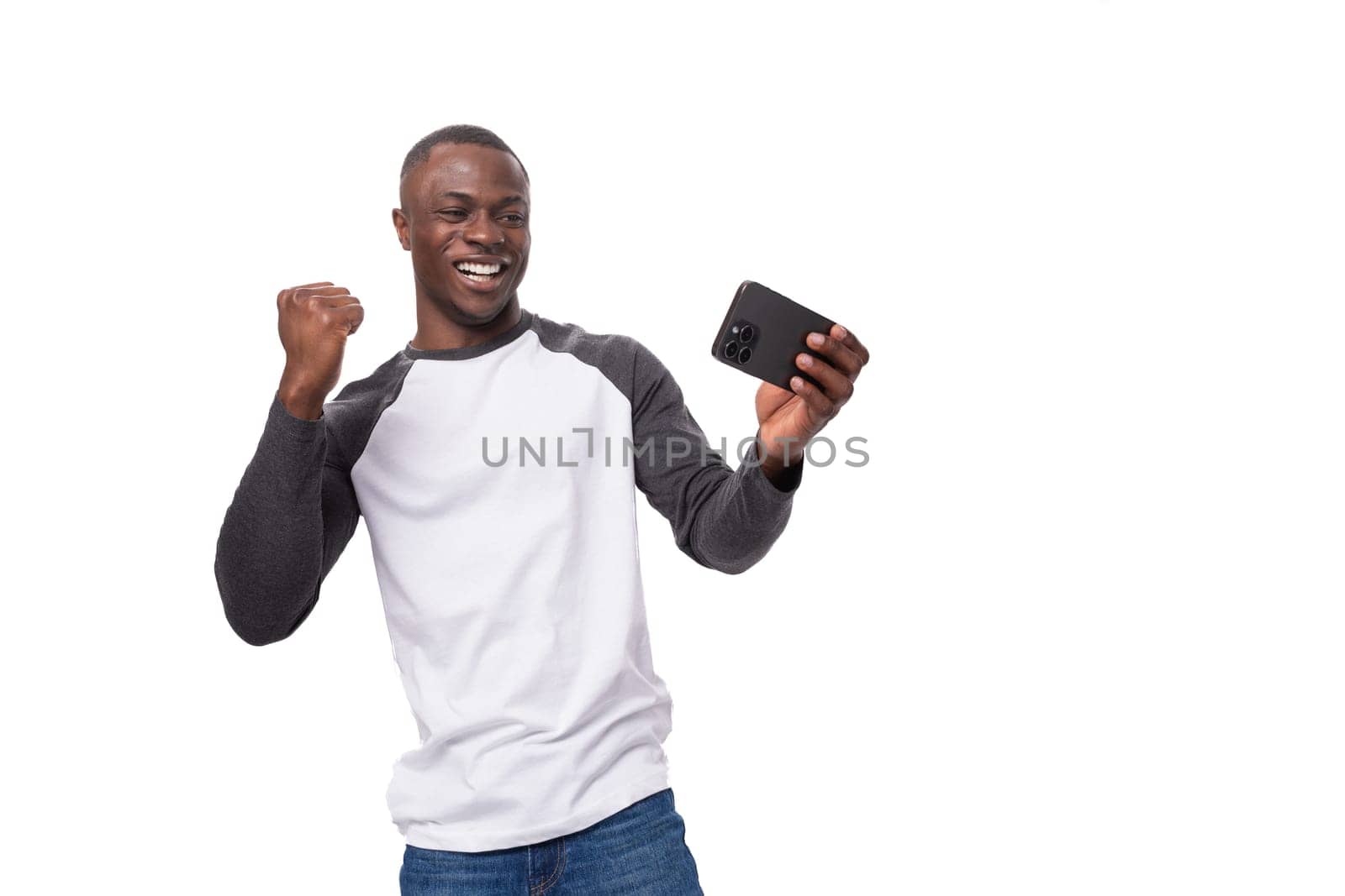 young positive african man dressed in a spring jacket feels joy holding a smartphone.