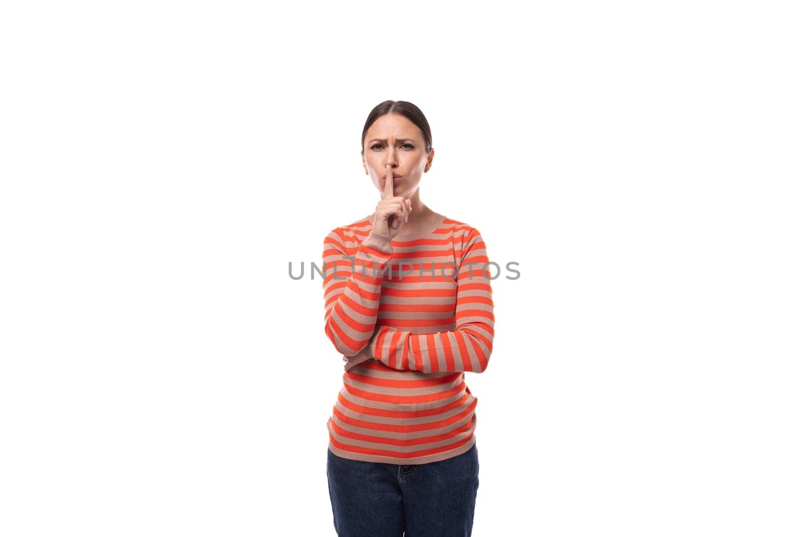 Young smart slim brunette woman dressed in a striped orange blouse and jeans on a white background by TRMK