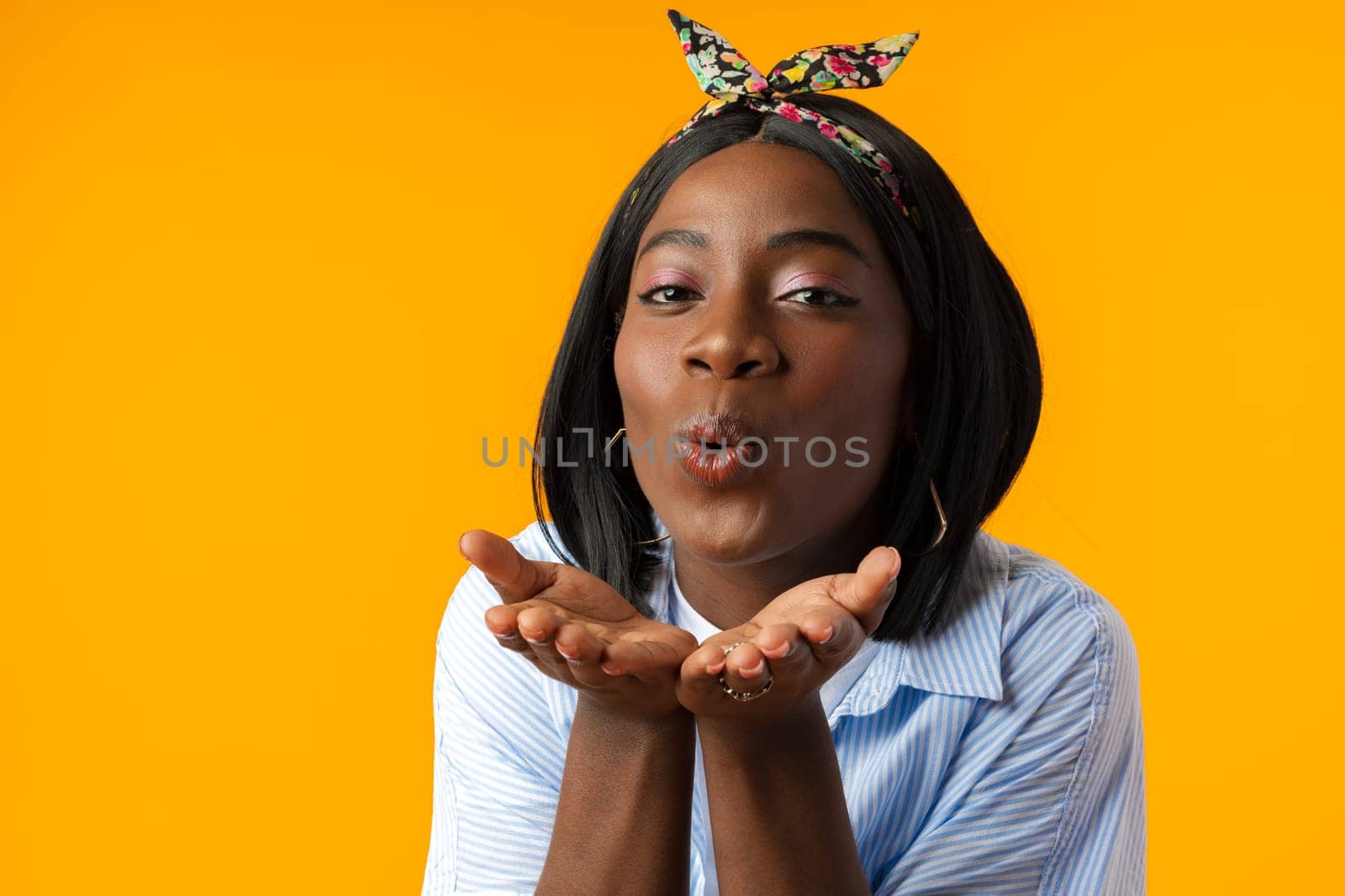 Portrait of a beautiful african woman blowing kiss to camera against yellow background
