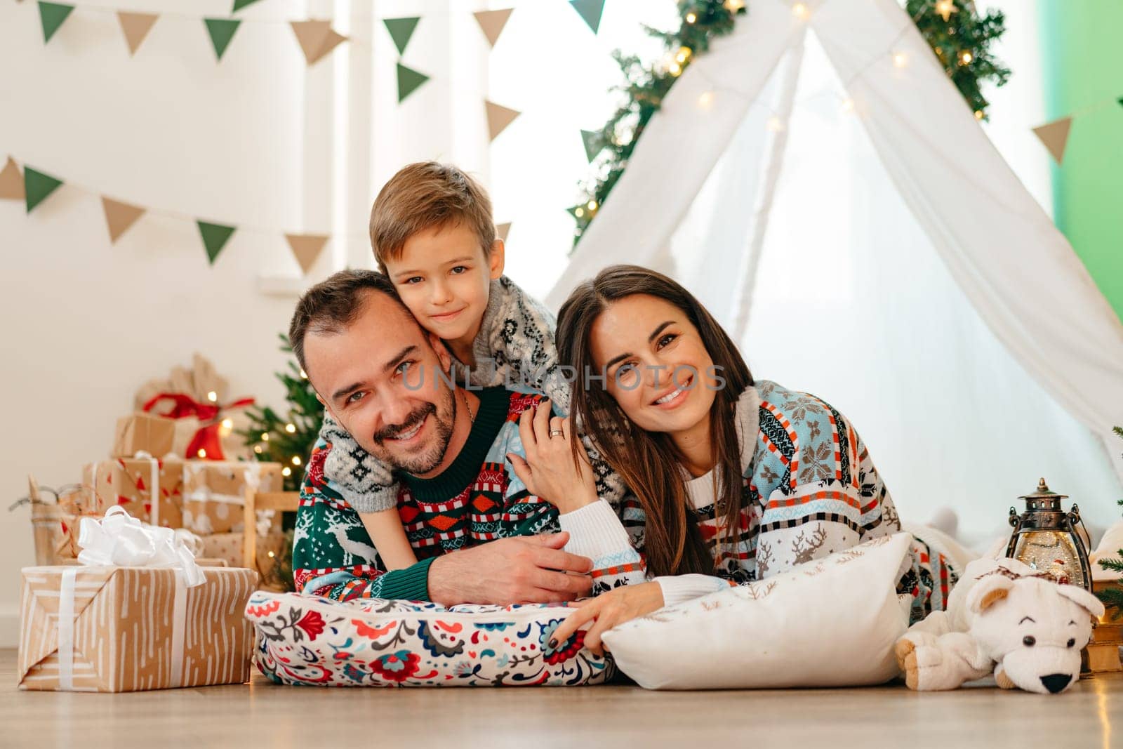 Happy parents play with their little son in a teepee during Christmas holidays, close up