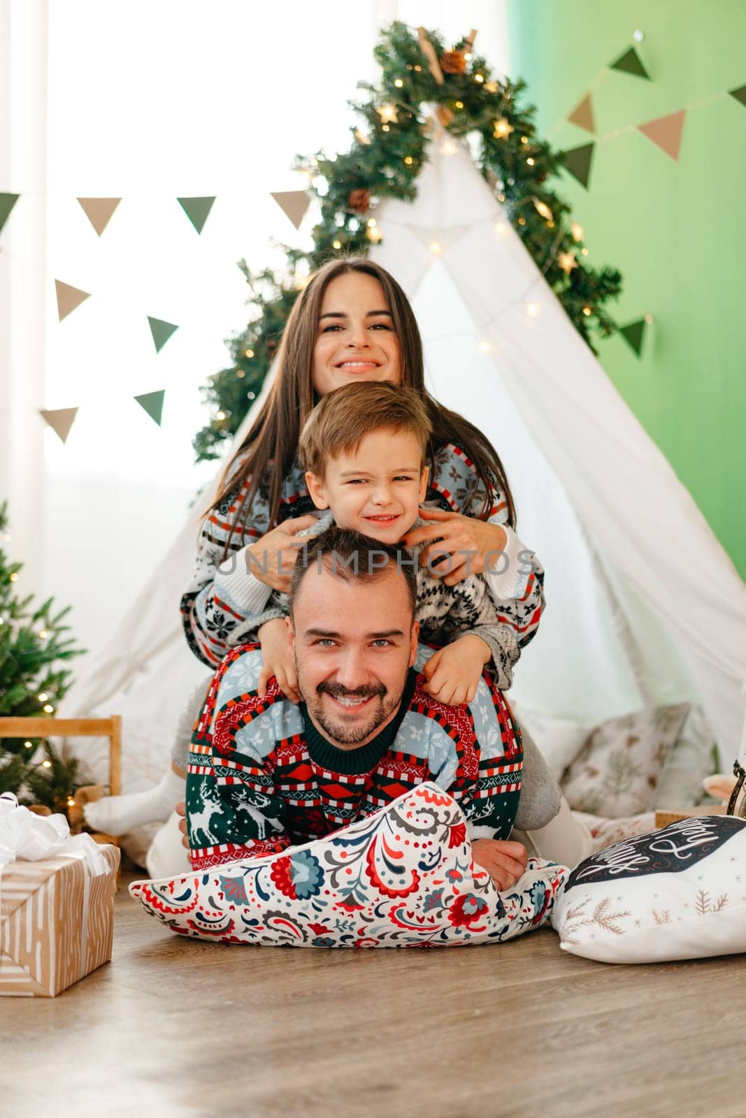 Happy parents play with their little son in a teepee during Christmas holidays, close up