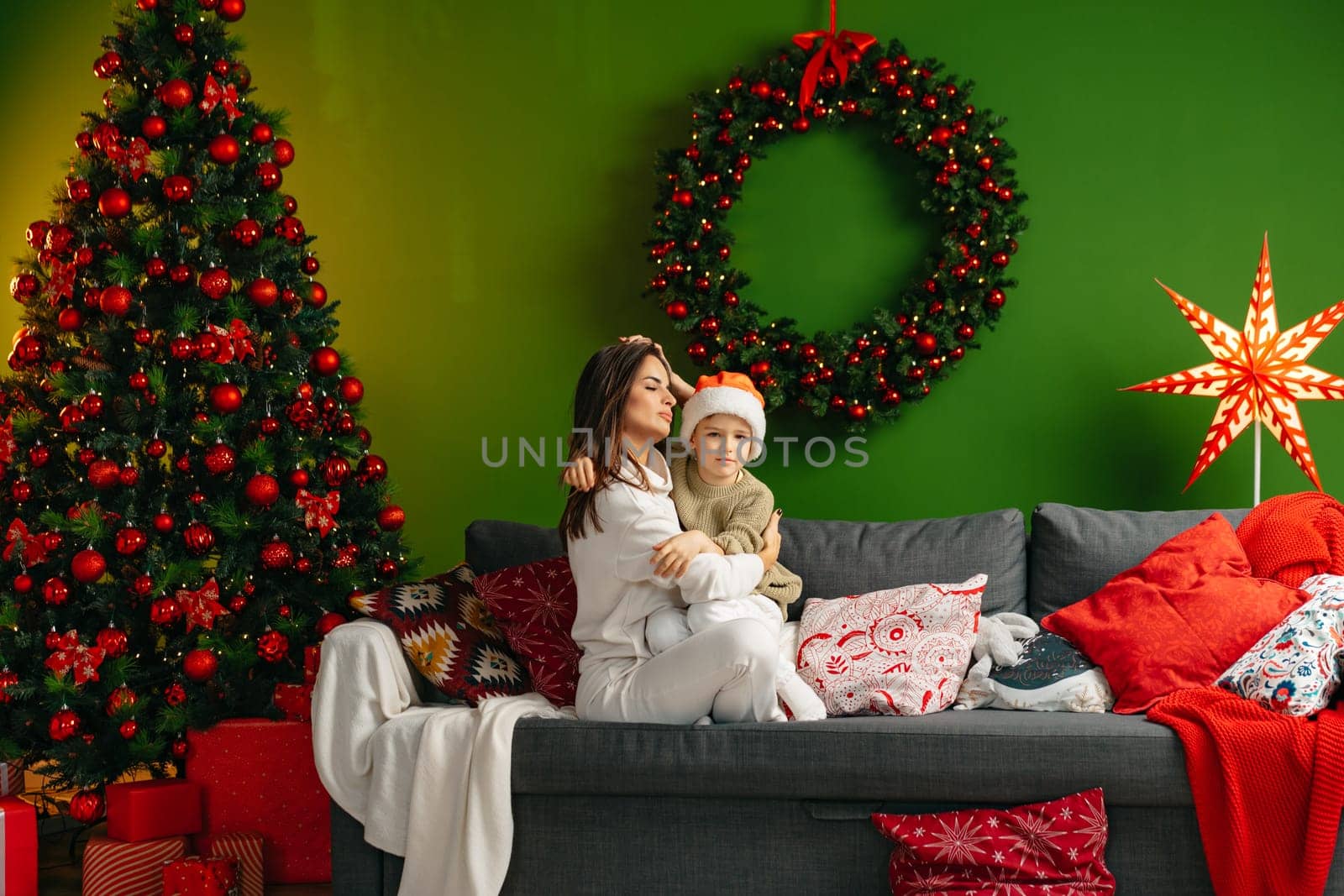 Mother sitting on a sofa with her son in living room decorated for Christmas by Fabrikasimf