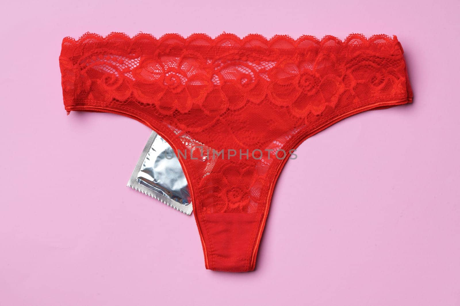 Beautiful women's panties with a condom on a paper background in studio. Safe intimate relationships concept