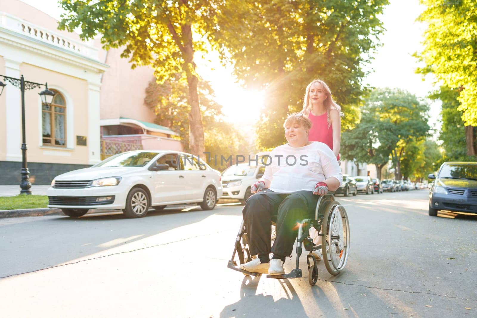 Young female caregiver pushing wheelchair with mature female person with disability across city street