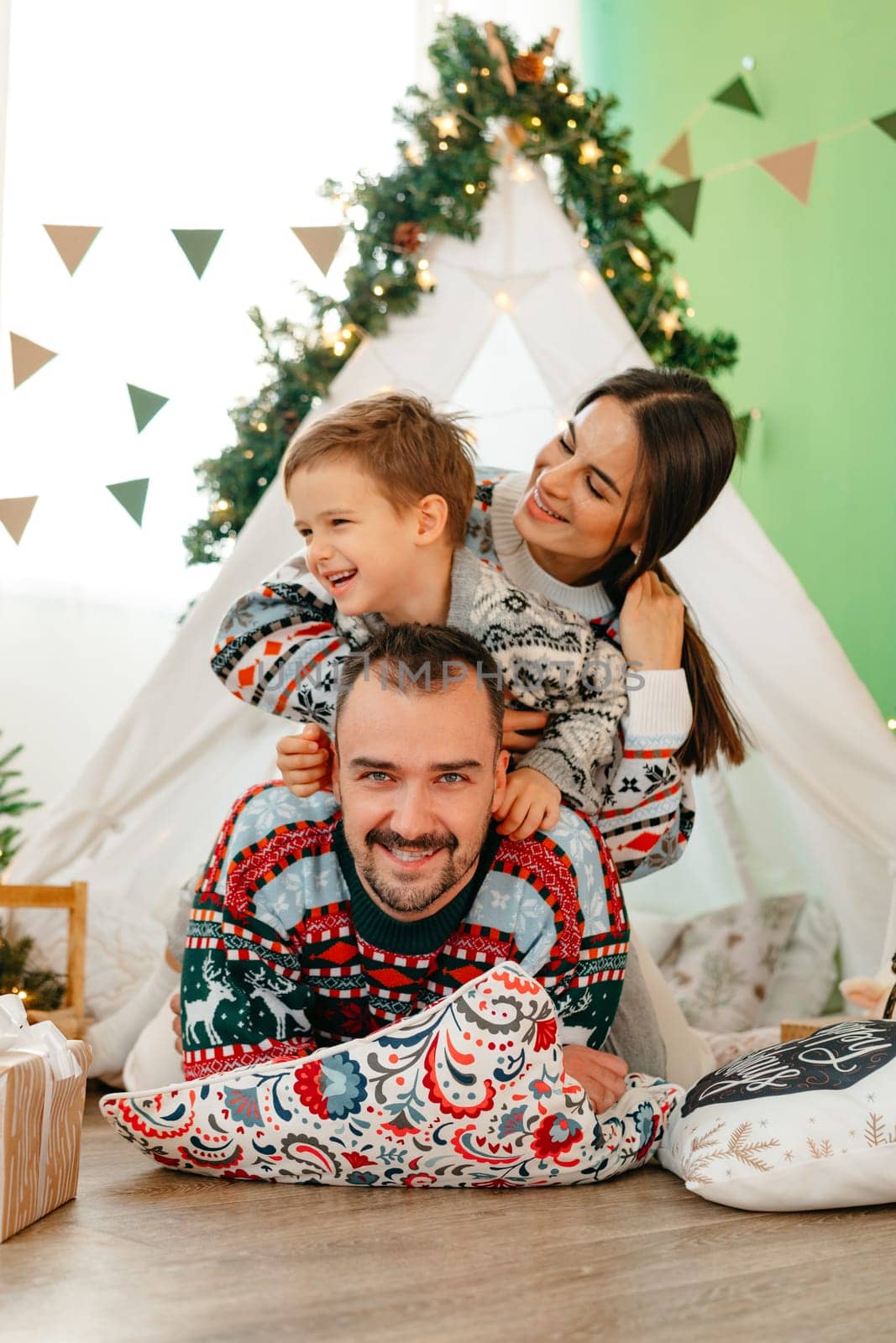 Happy parents play with their little son in a teepee during Christmas holidays by Fabrikasimf
