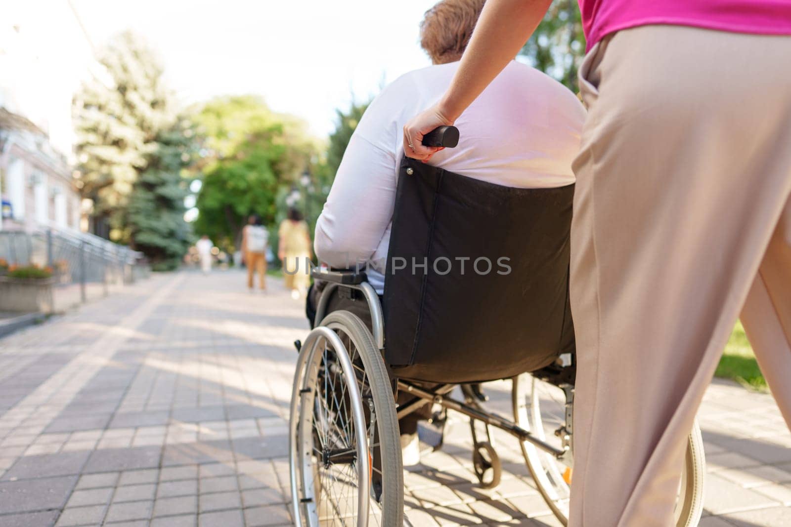 Young female caregiver pushing wheelchair with mature female person with disability across city street