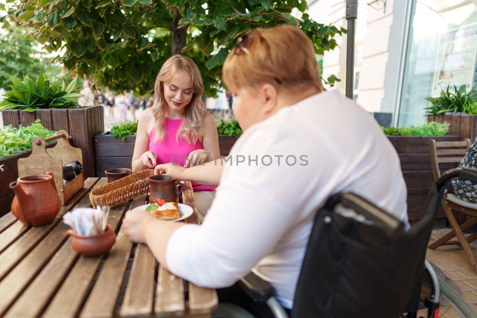 Woman wheelchair user dining at a restaurant with her young daughter. by Fabrikasimf