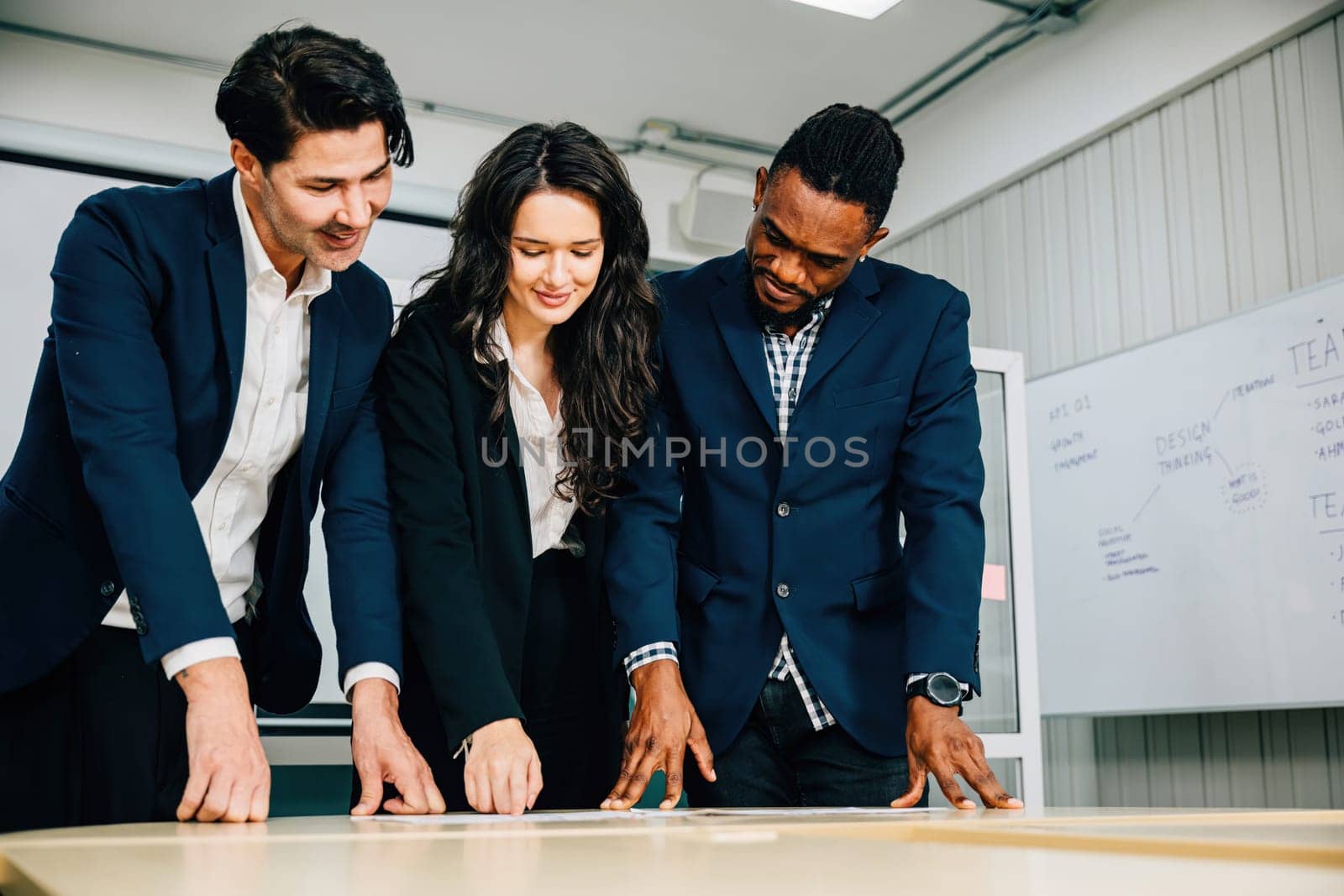 Colleagues at a conference room desk stand, actively planning for business success. Teamwork, diversity, and leadership define this successful meeting. by Sorapop