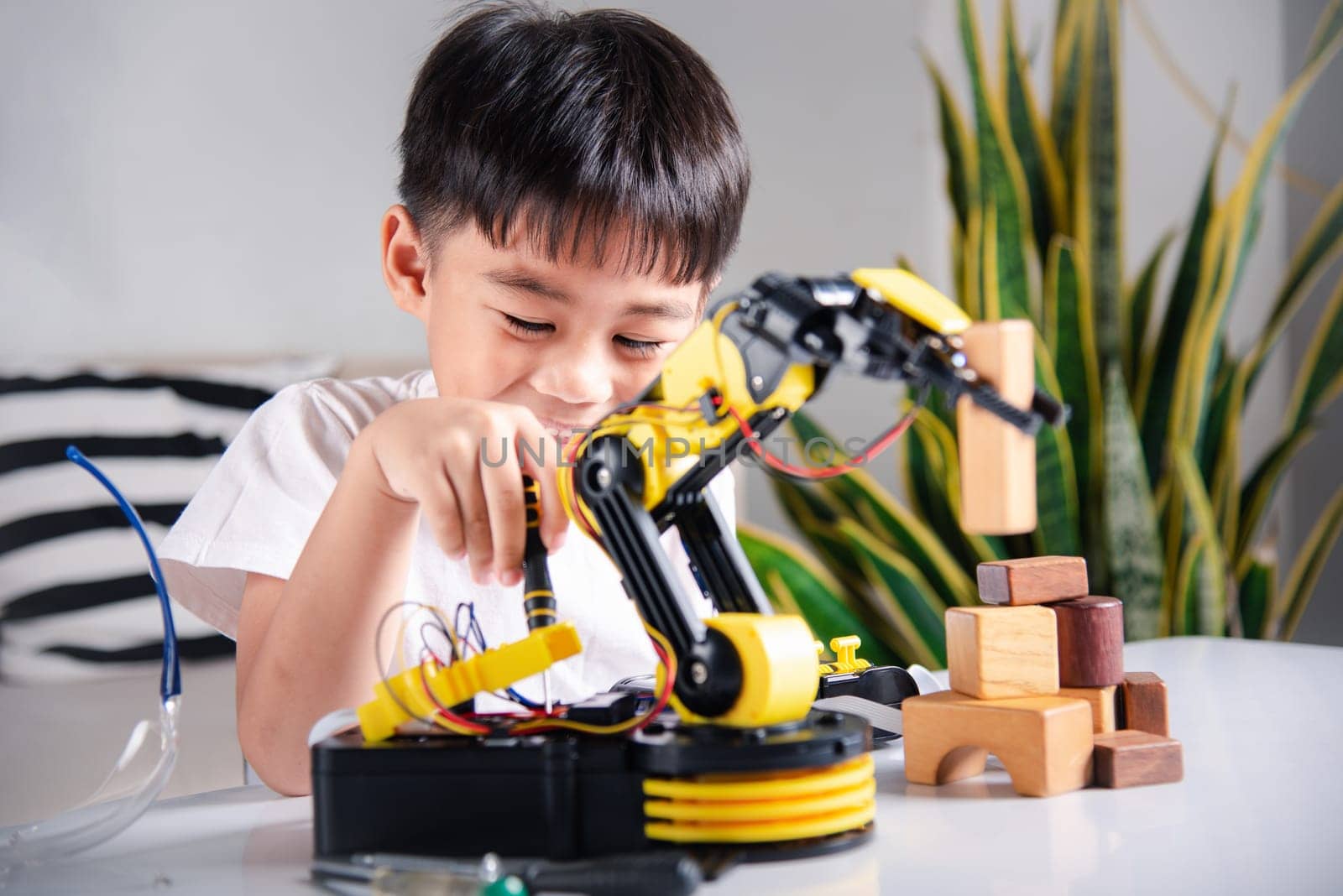 Happy Asian little kid boy using screwdriver to fixes screws robotic machine arm in home workshop by Sorapop