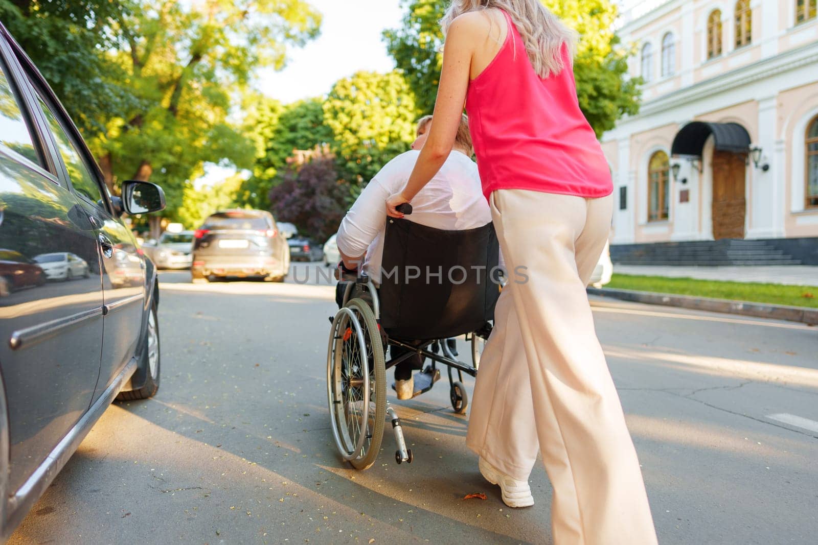 Young female caregiver pushing wheelchair with mature female person with disability across city street