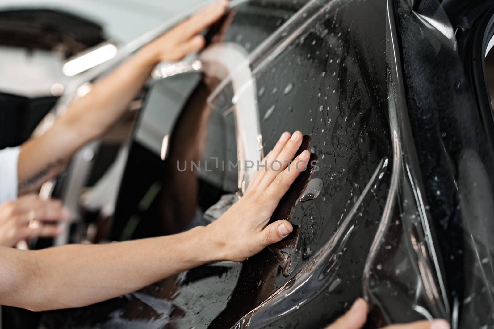 Car wrapping specialist wraps a car with adhesive film in car detailing service, close up