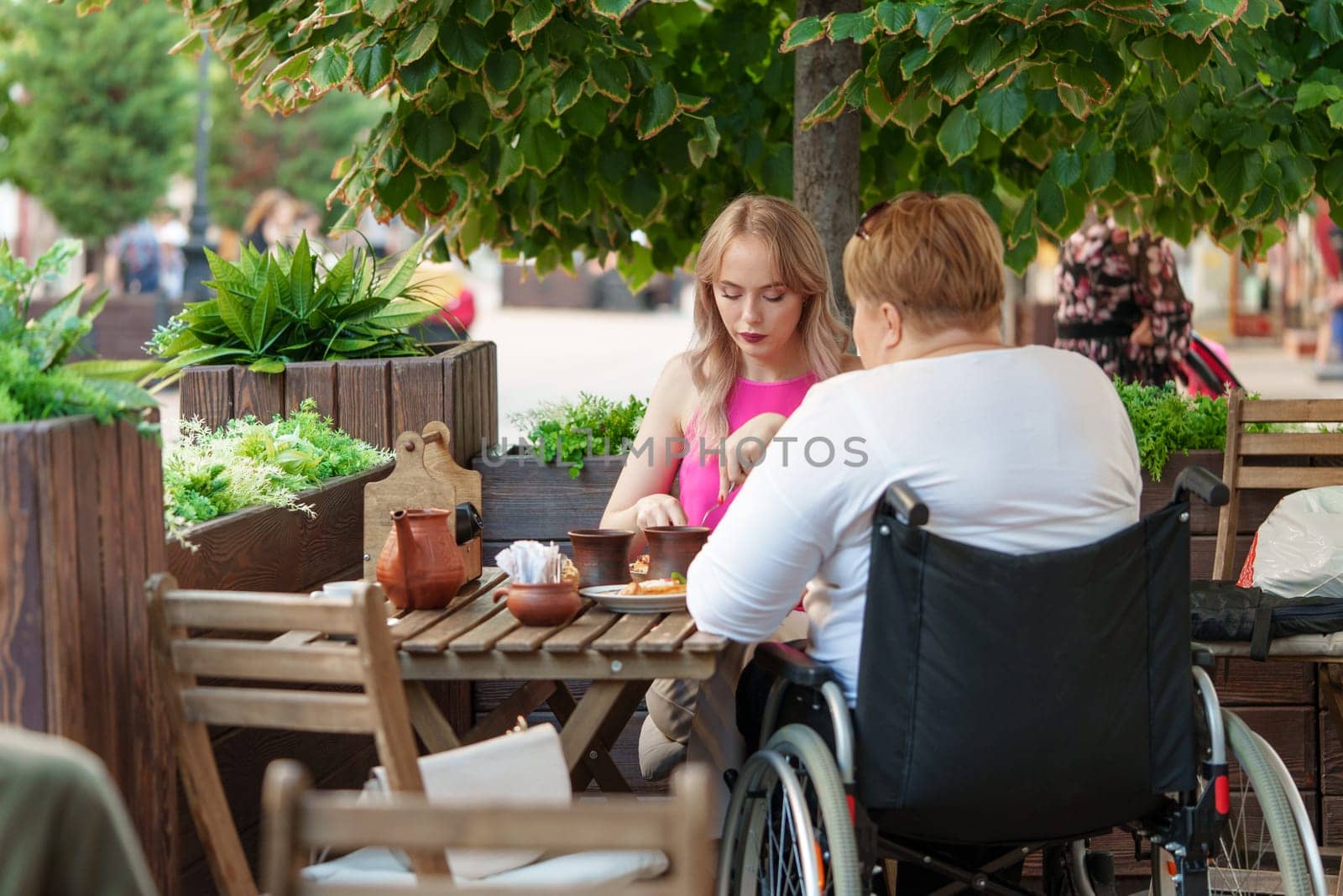 Woman wheelchair user dining at a restaurant with her young daughter. by Fabrikasimf