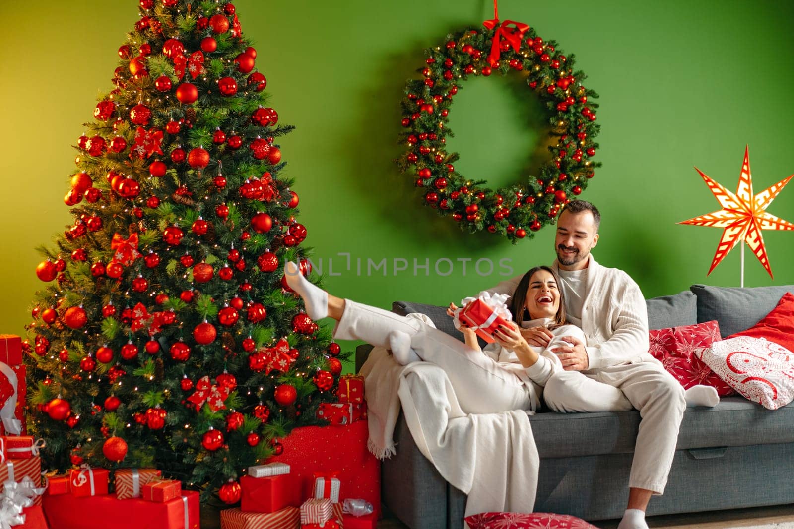 Happy young couple sitting on sofa on Christmas eve at home by Fabrikasimf