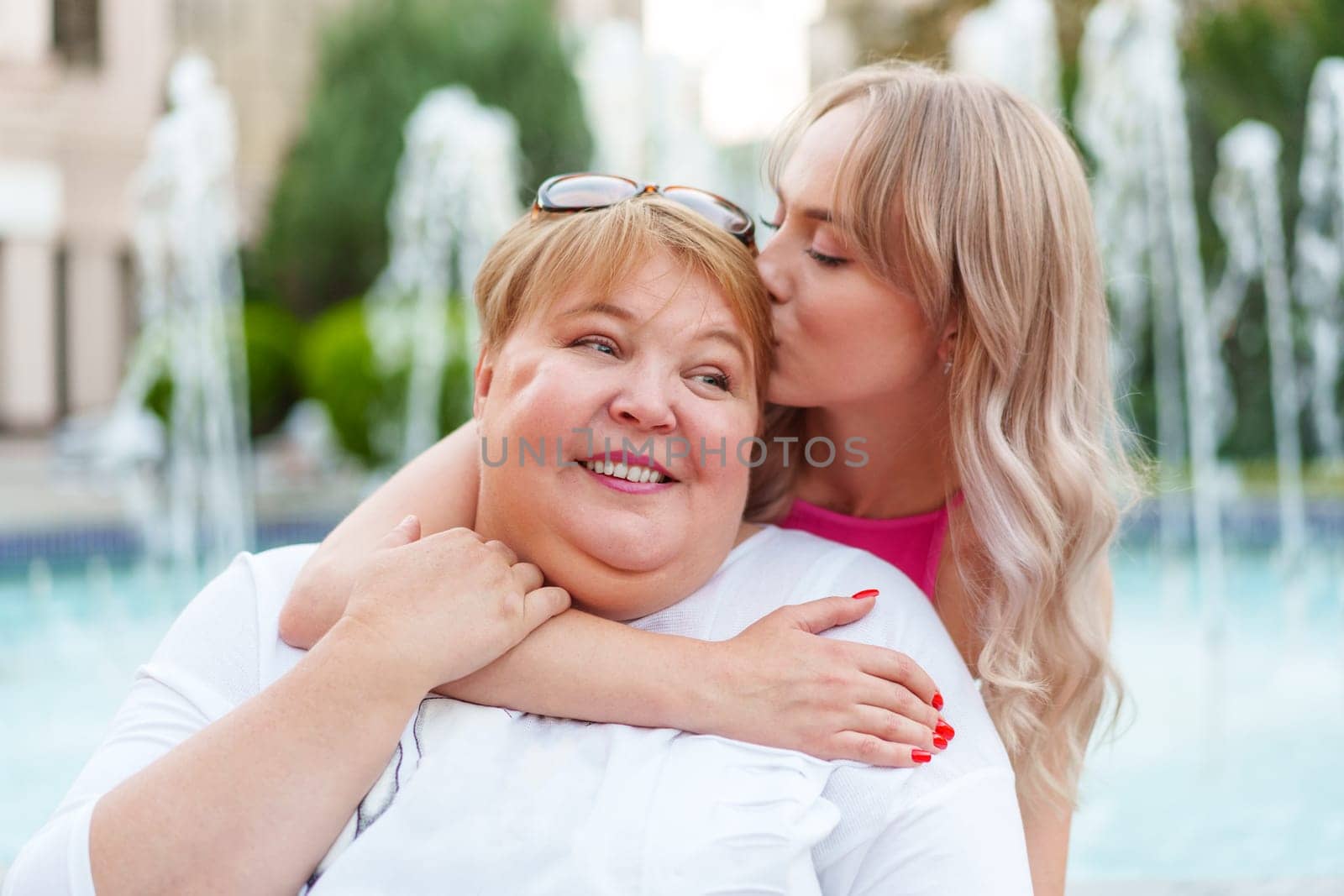 Positive young woman and her mother embracing on city street by Fabrikasimf