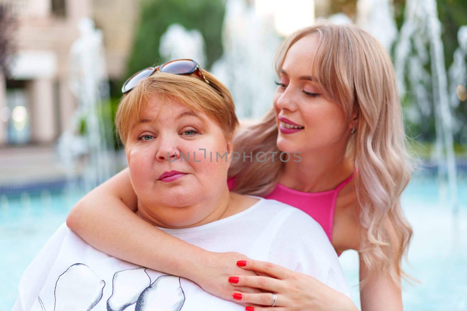 Positive young woman and her mother embracing on city street close up