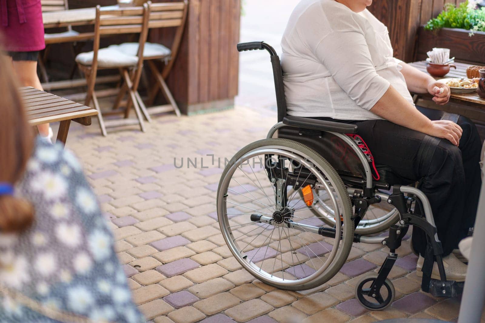 Unrecognizable woman with disability sitting in wheelchair in the street close up by Fabrikasimf