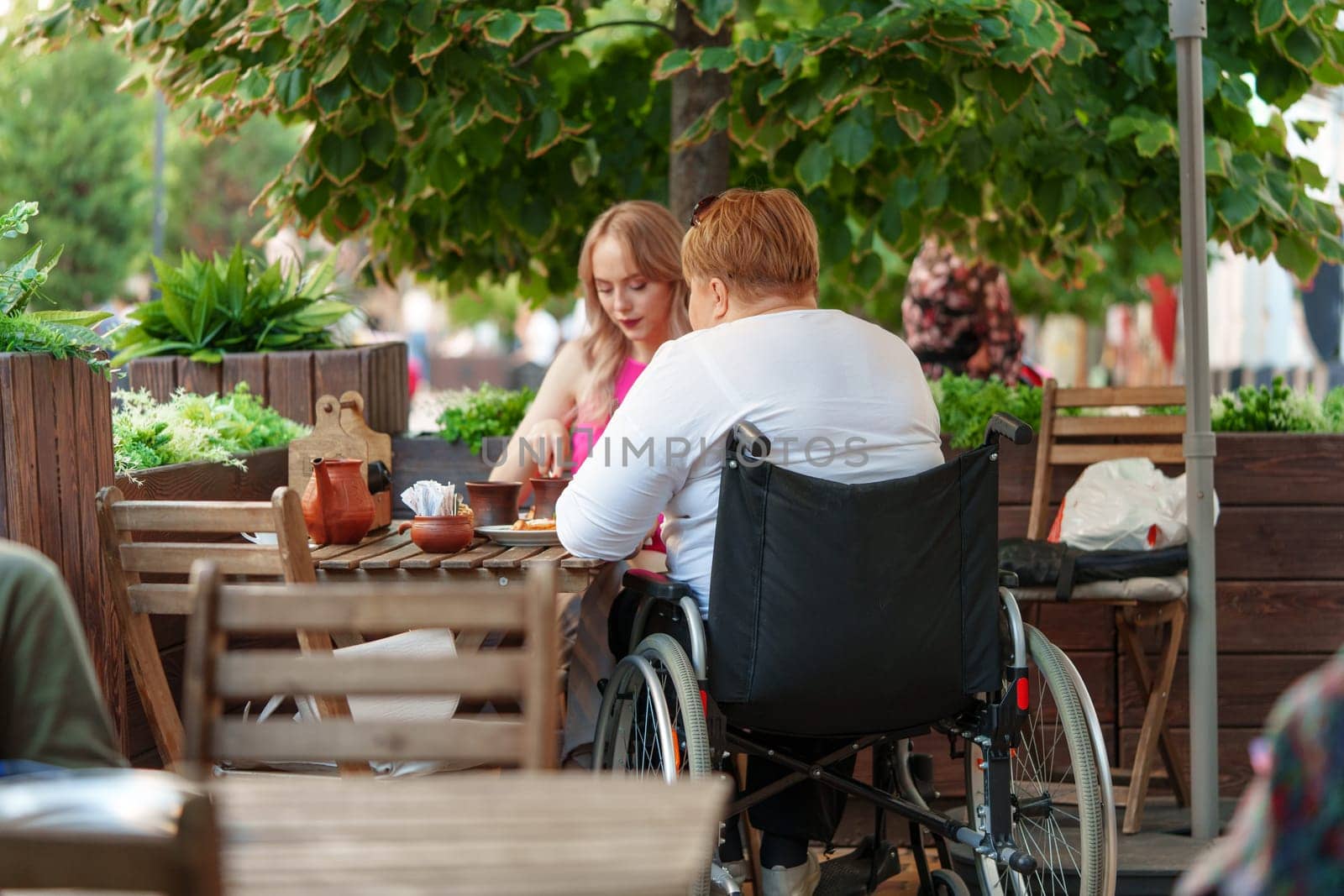 Woman wheelchair user dining at a restaurant with her young daughter. by Fabrikasimf