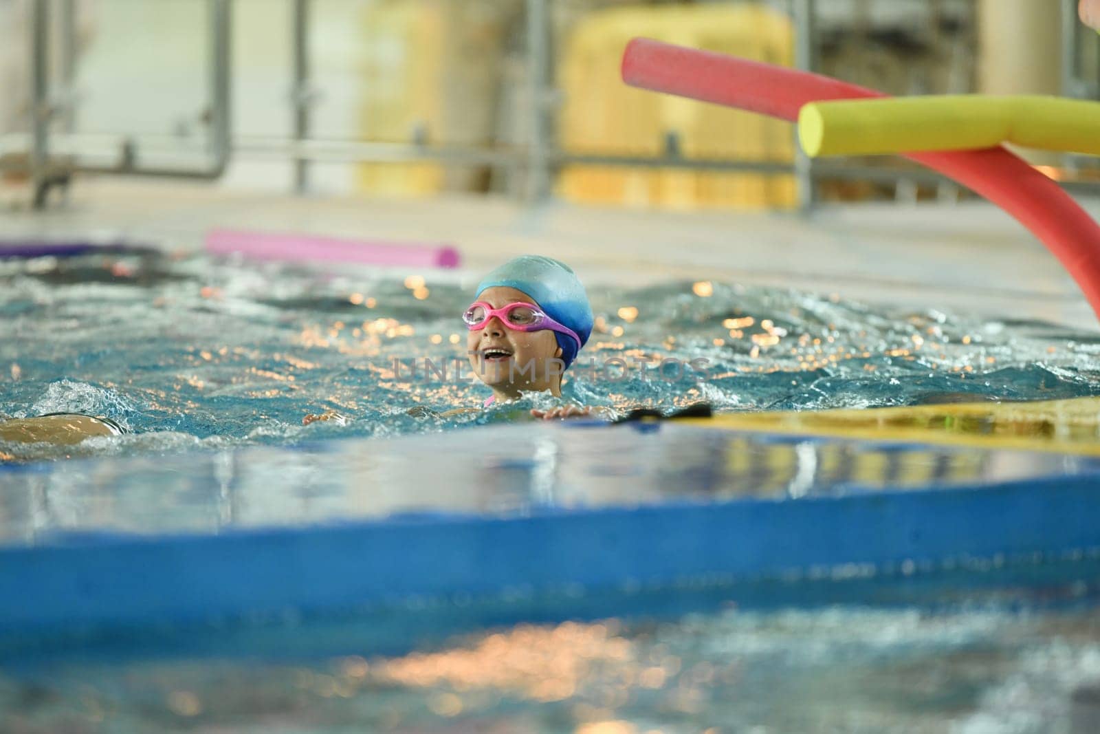 A child in a silicone cap and glasses learns to swim in the pool by Godi