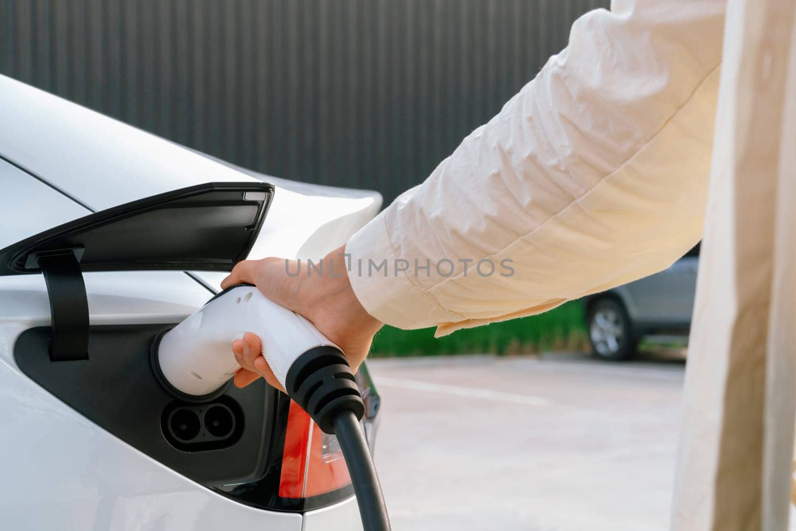 Young woman put EV charger to recharge electric car's battery from charging station. Alternative energy and rechargeable EV car for sustainable environmental friendly travel concept. Expedient