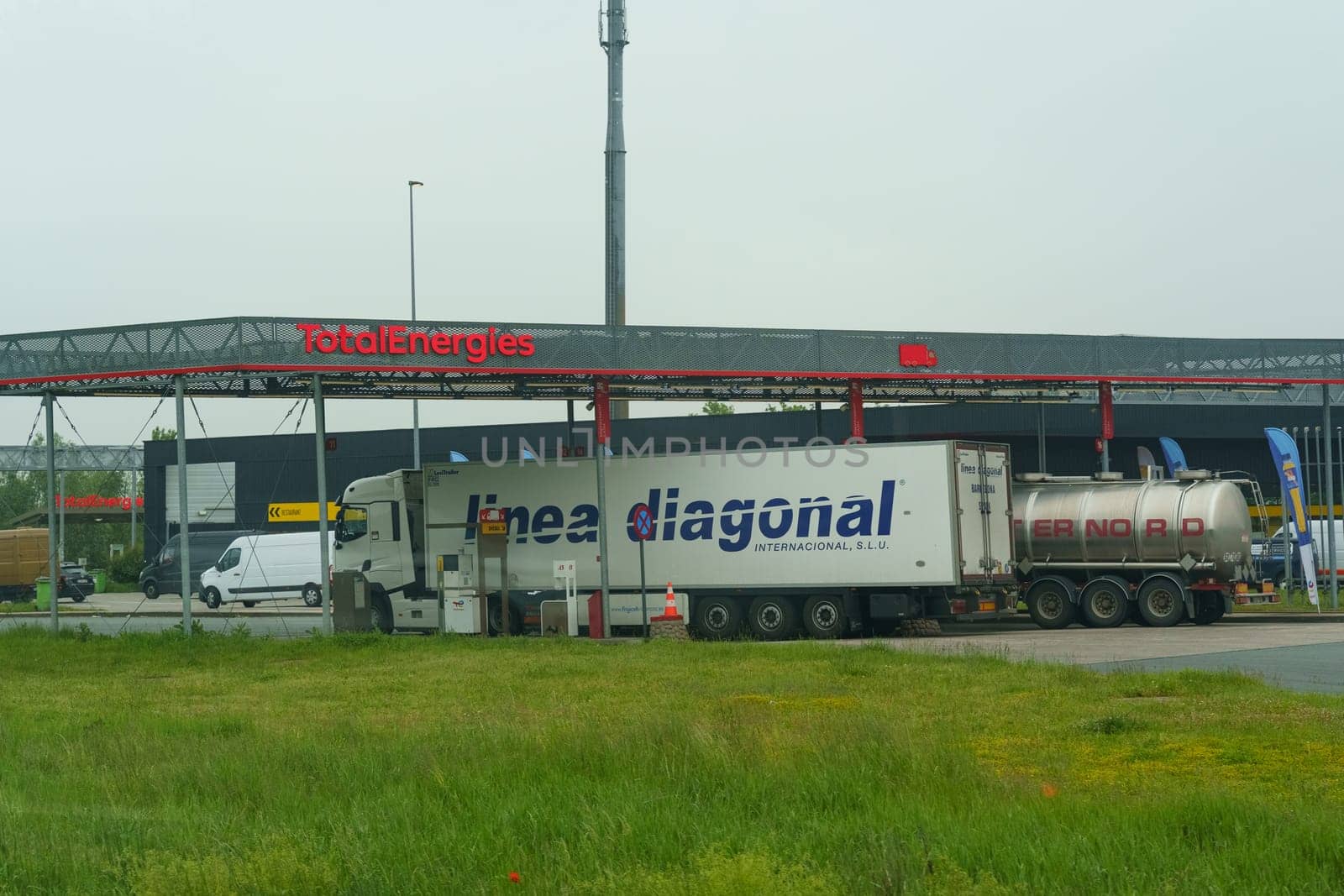 Waregem, Belgium - May 22, 2023: A commercial truck parked in front of a gas station, with a fuel pump nearby and signage for services offered.