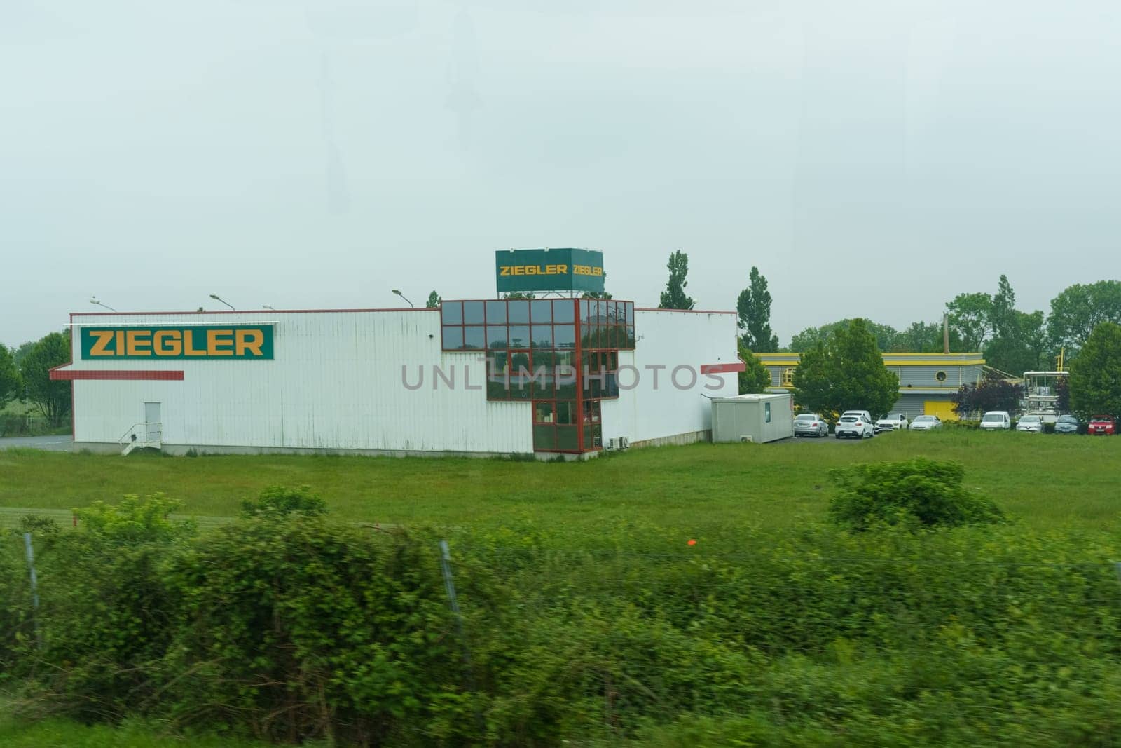 Orly, France - May 23, 2023: The Ziegler building stands beside a road, partly obscured by greenery, with the glimpse of a clear sky and other establishments in the distance.