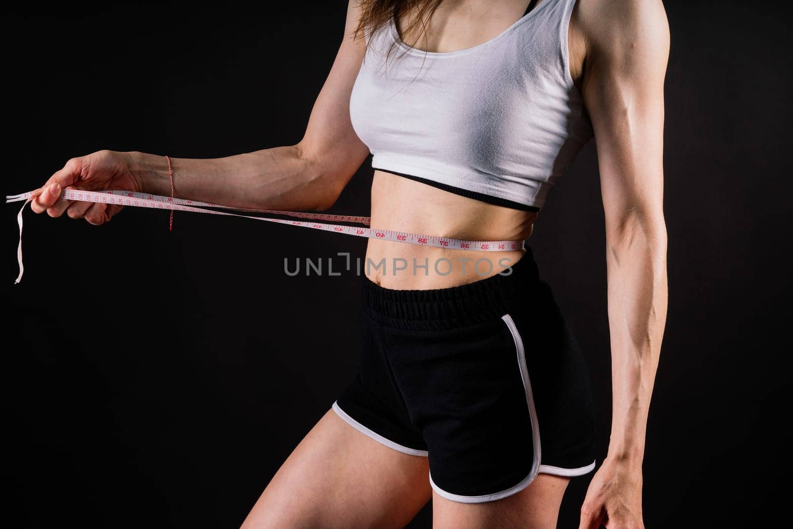 Athletic slim woman measuring her waist by measure tape after a diet over dark yellow background by Zelenin