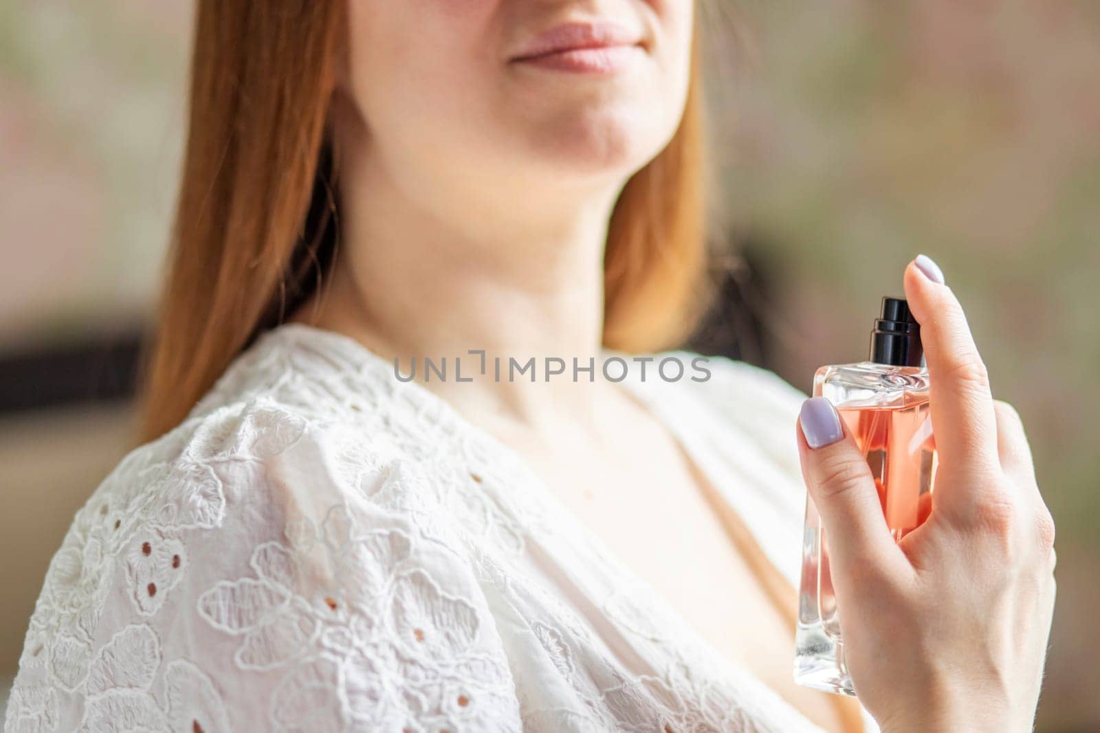 Woman holding a perfume bottle in a white lace dress. Studio shot with a shallow depth of field, beauty and fashion concept for design and print.