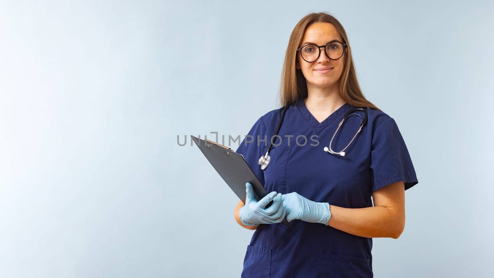 Smiling female healthcare worker in blue scrubs with clipboard. Professional medical staff portrait for healthcare design and poster.