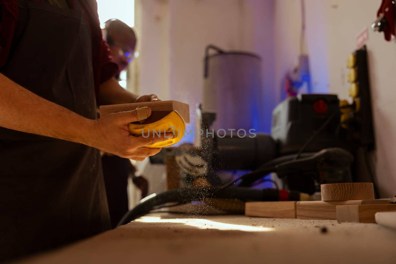 Man at workbench using manual sandpaper tool to sander timber block, assembling furniture in carpentry shop. Carpenter smoothing piece of wood, improving its appearance, close up shot