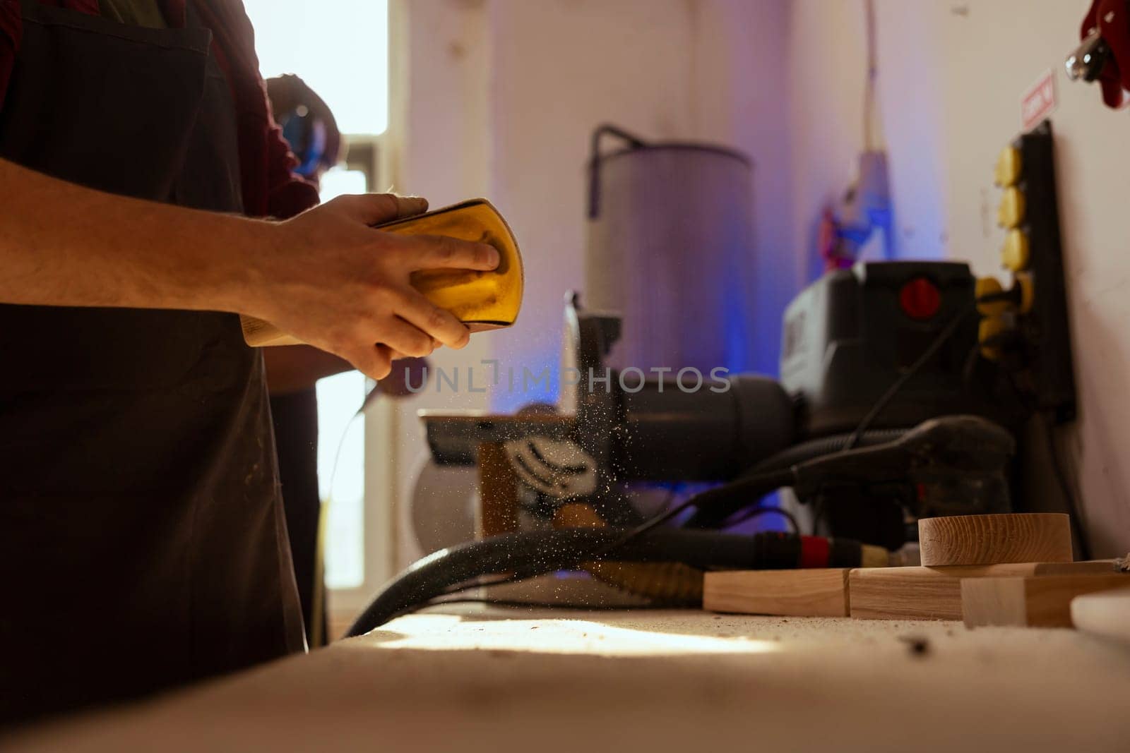 Woodworker working in carpentry shop using sanding block to remove imperfections on wood piece. Carpenter using coarse grade sandpaper to do manual sanding, close up shot