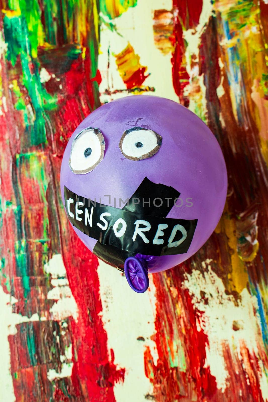 In a vivid juxtaposition of color and constraint, behold this symbolic image featuring a balloon with its mouth taped shut, suspended against a backdrop of vibrant, colorful painting