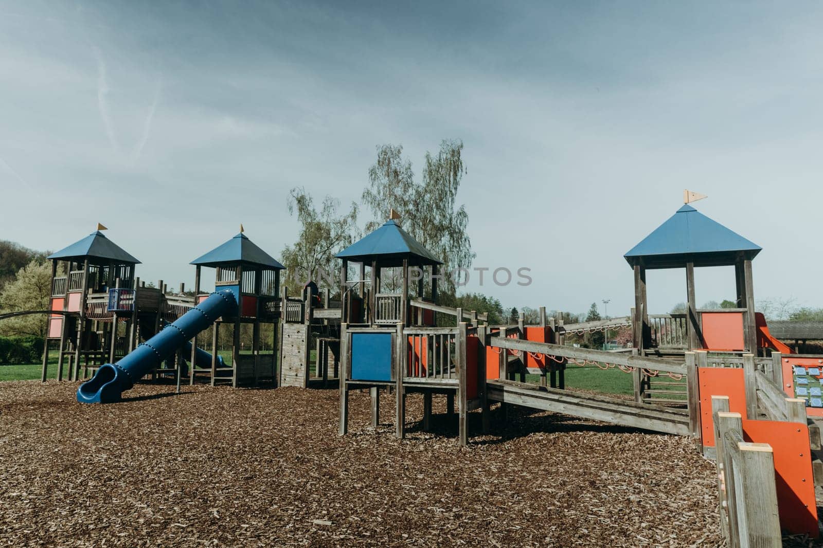 Beautiful view of an empty playground with wooden houses, ropeways and plastic pipes and slides on a sunny spring day in a public park, close-up side view.