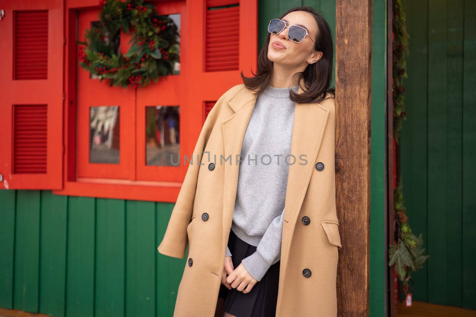 People, season and Christmas concept portrait of happy smiling middle age woman outdoors dressed stylish cream trench coat with Christmas festive decoration on background. Free space