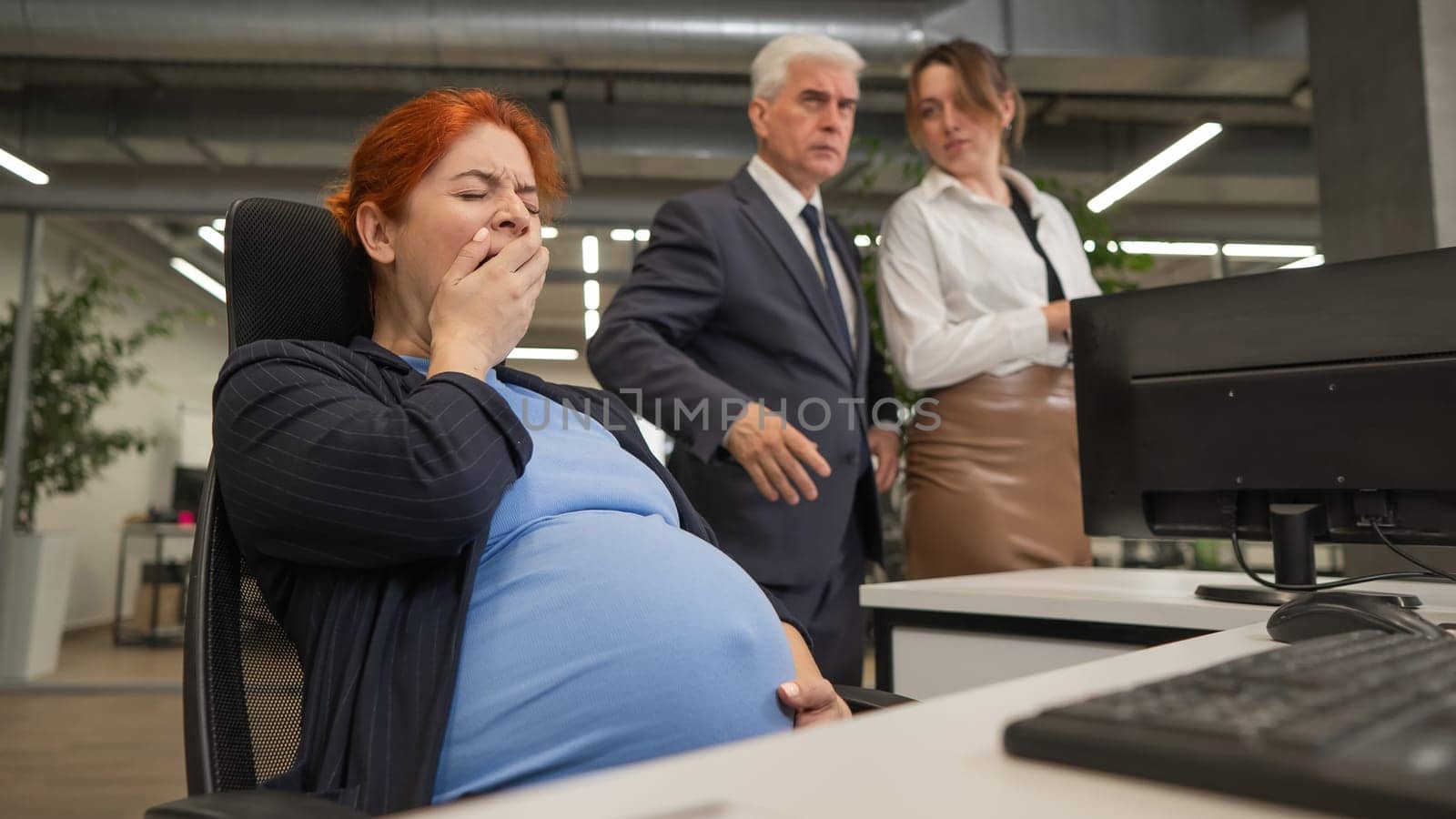 Pregnant woman yawns at work. Colleagues look disapprovingly. by mrwed54