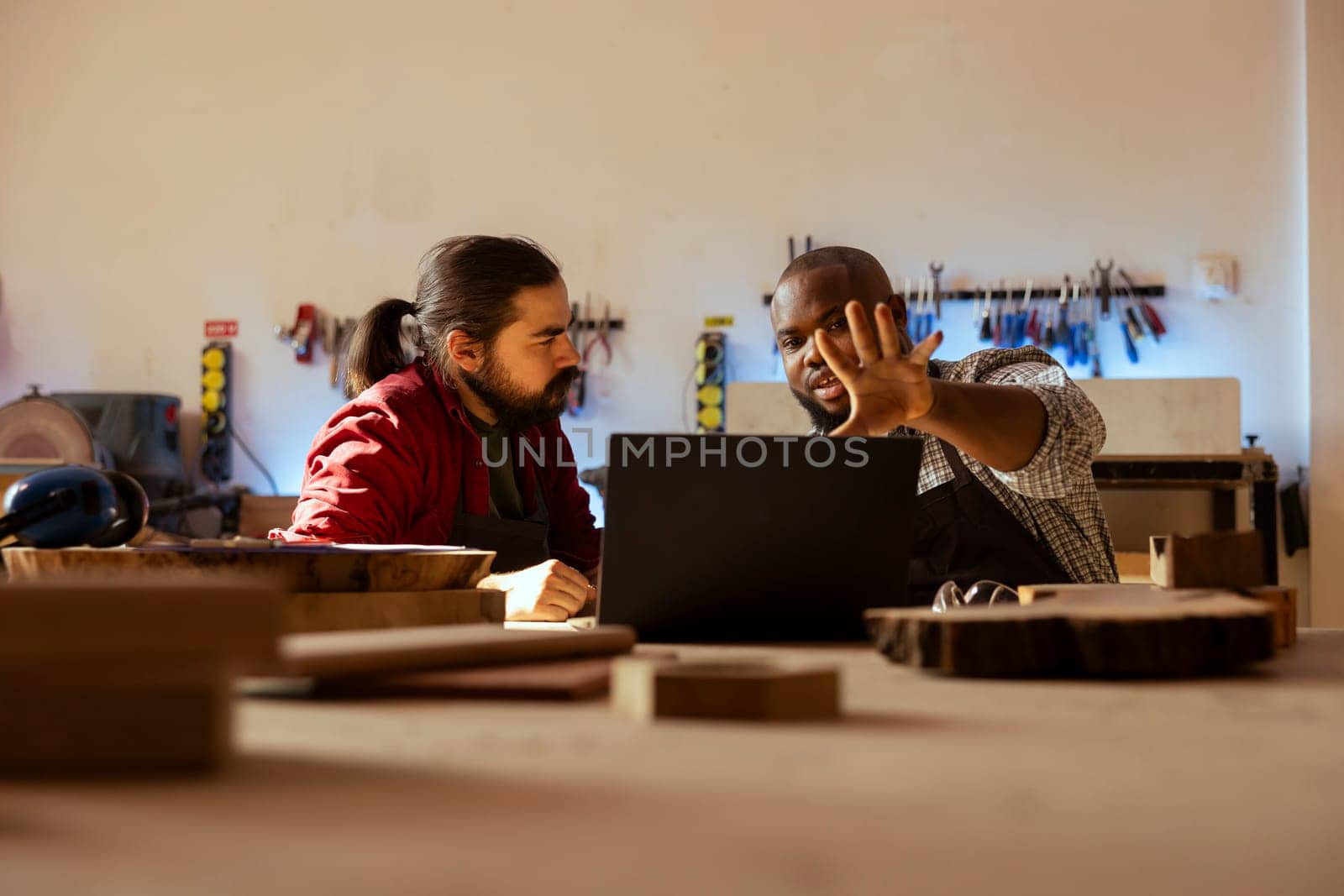 Cabinetmakers doing brainstorming while using CAD software on laptop, discussing wood designs. Carpenters in assembly shop discussing, using program on notebook to plan furniture assembling