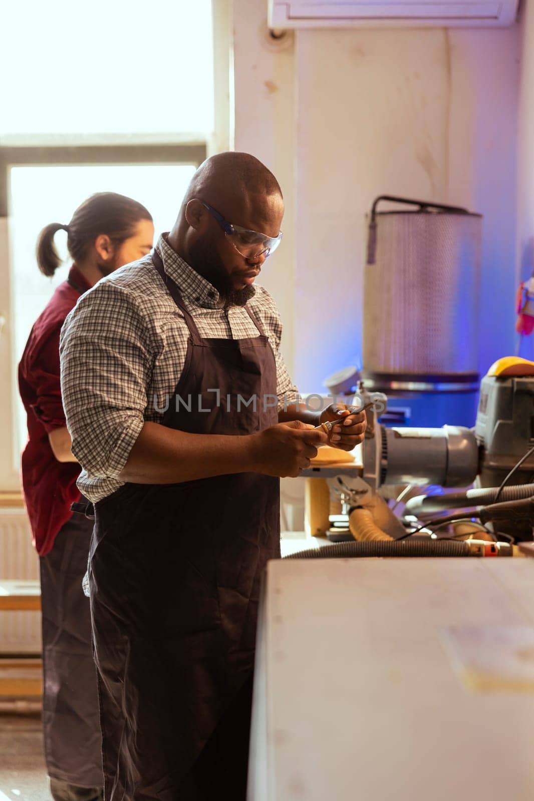 African american carpenter looking at screwdriver, preparing to start production in furniture assembly shop. BIPOC cabinetmaker at workbench inspecting tool, ready to work on wood designs