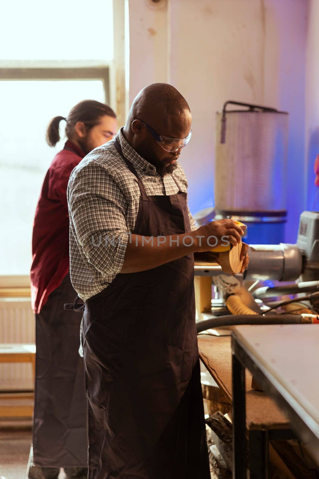 African american artisan in studio using sandpaper for smoothing wooden surface, creating wood art designs. BIPOC person using sanding sheets to refurbish damages suffered by timber block