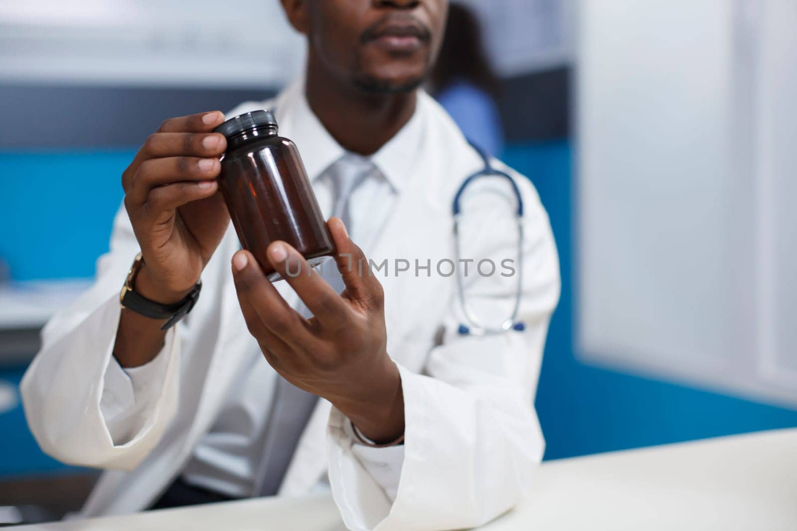 Close-up shot of a black man wearing a lab coat and holding a prescription medicine in the clinic office. Detailed image of African American doctor grasping a bottle of pills for recovery treatment.